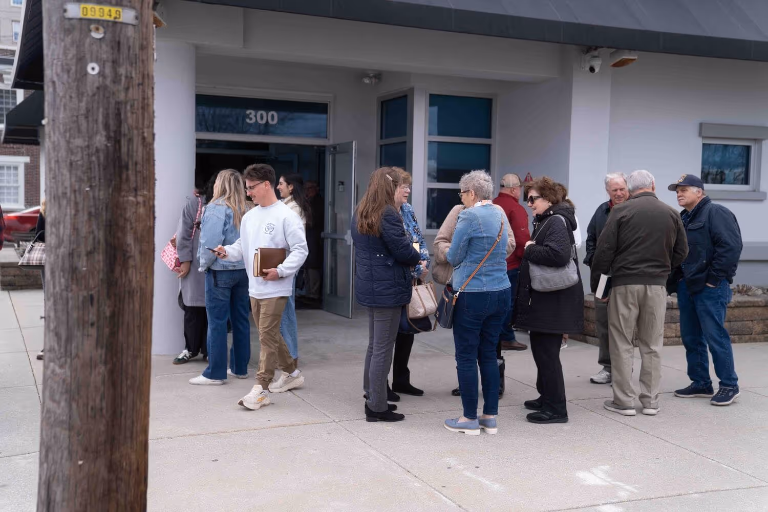 People gathered outside church building entrance, some holding books, wearing casual attire, near hospital.
