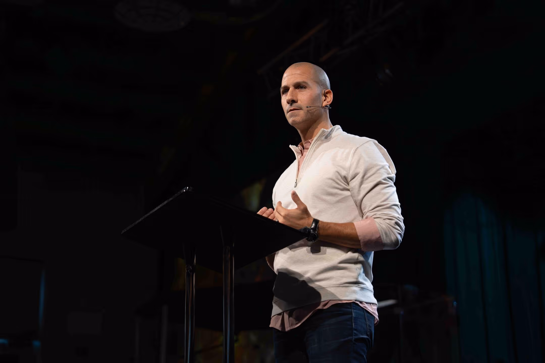 Man in white shirt speaking at podium with microphone in a church setting.