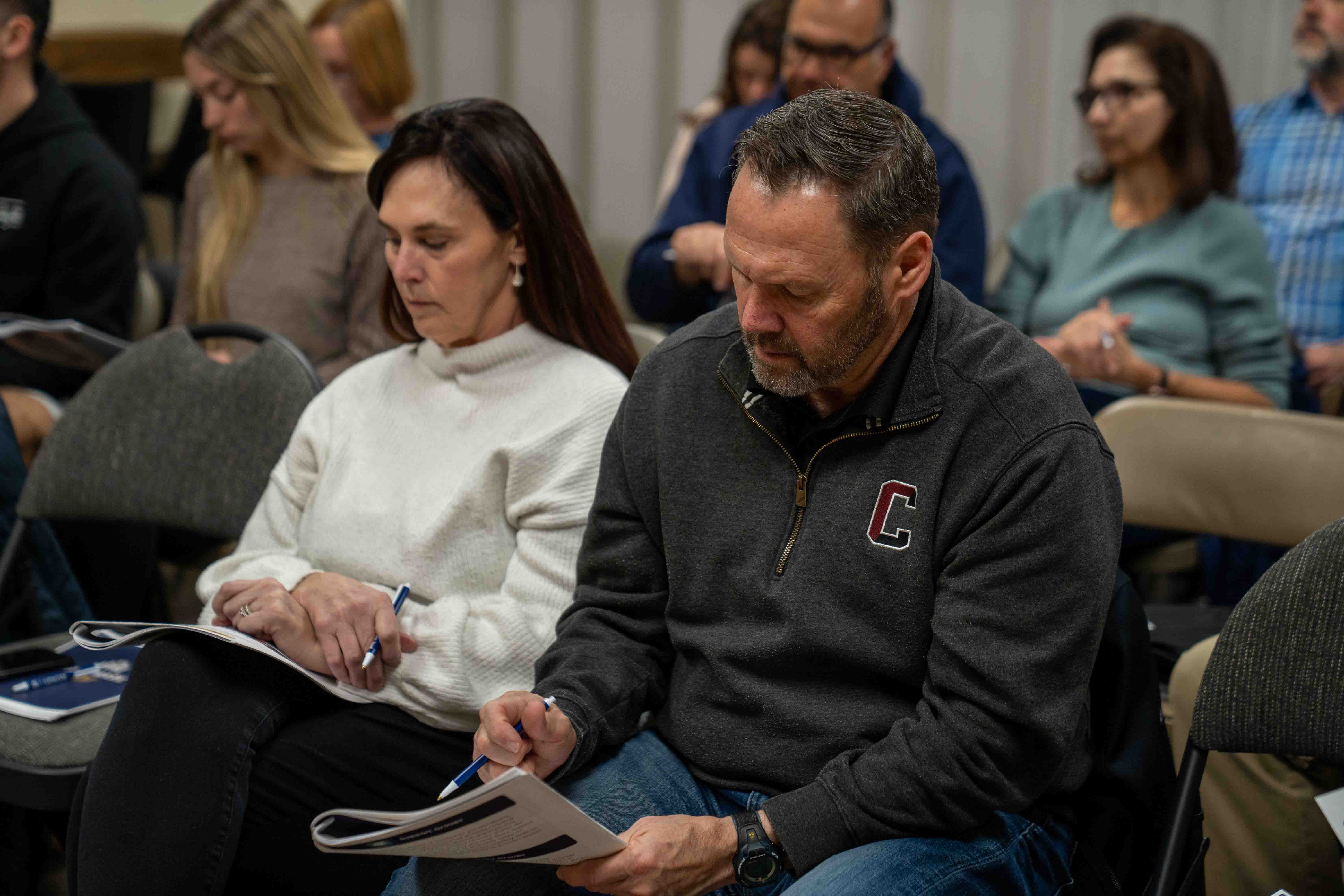 People sitting in church pews, taking notes during a religious organization meeting or hospital seminar.