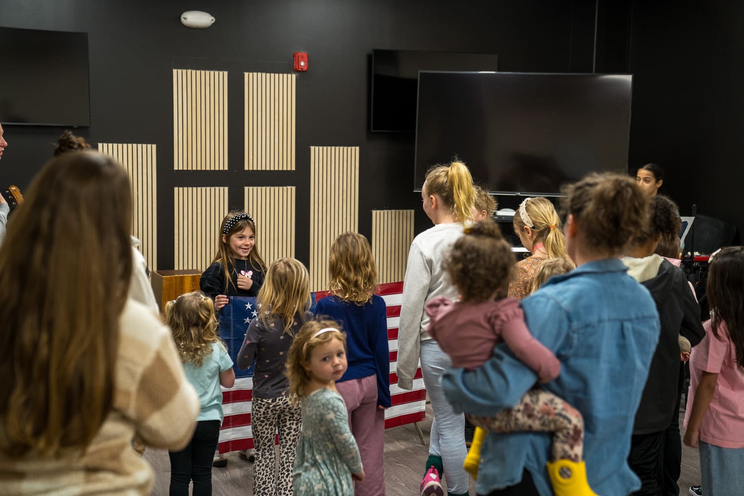 Children and adults gathered in church, reciting pledge allegiance to American flag.