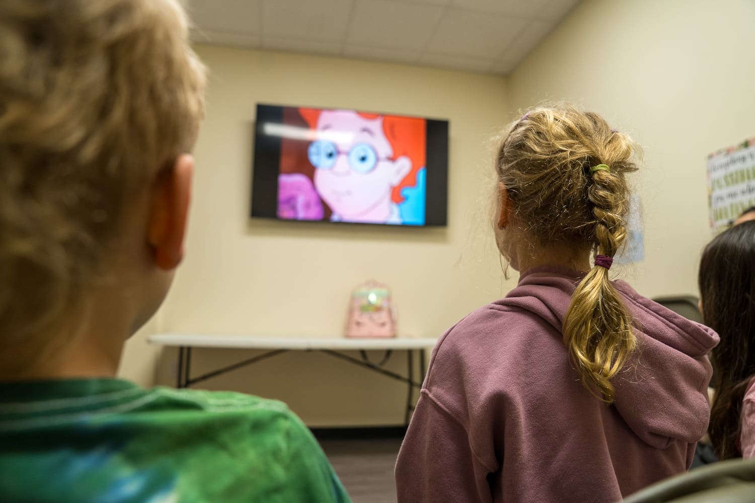 Children watching cartoon on TV in hospital or church community room setting.