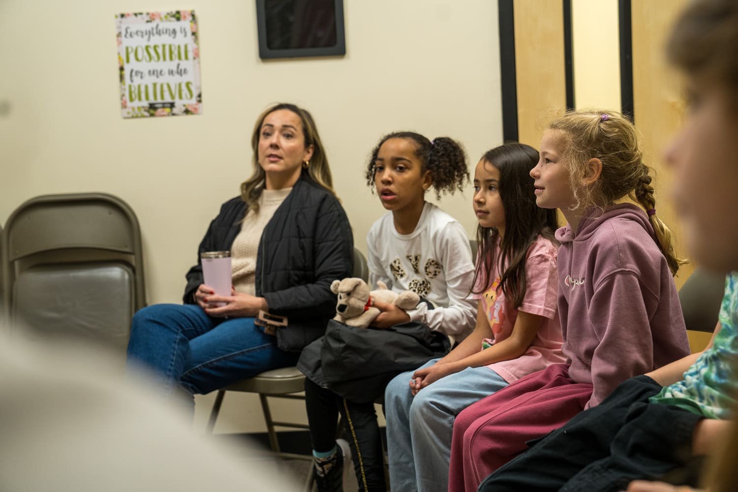 Woman and children sitting together in a hospital or church setting, looking attentive.