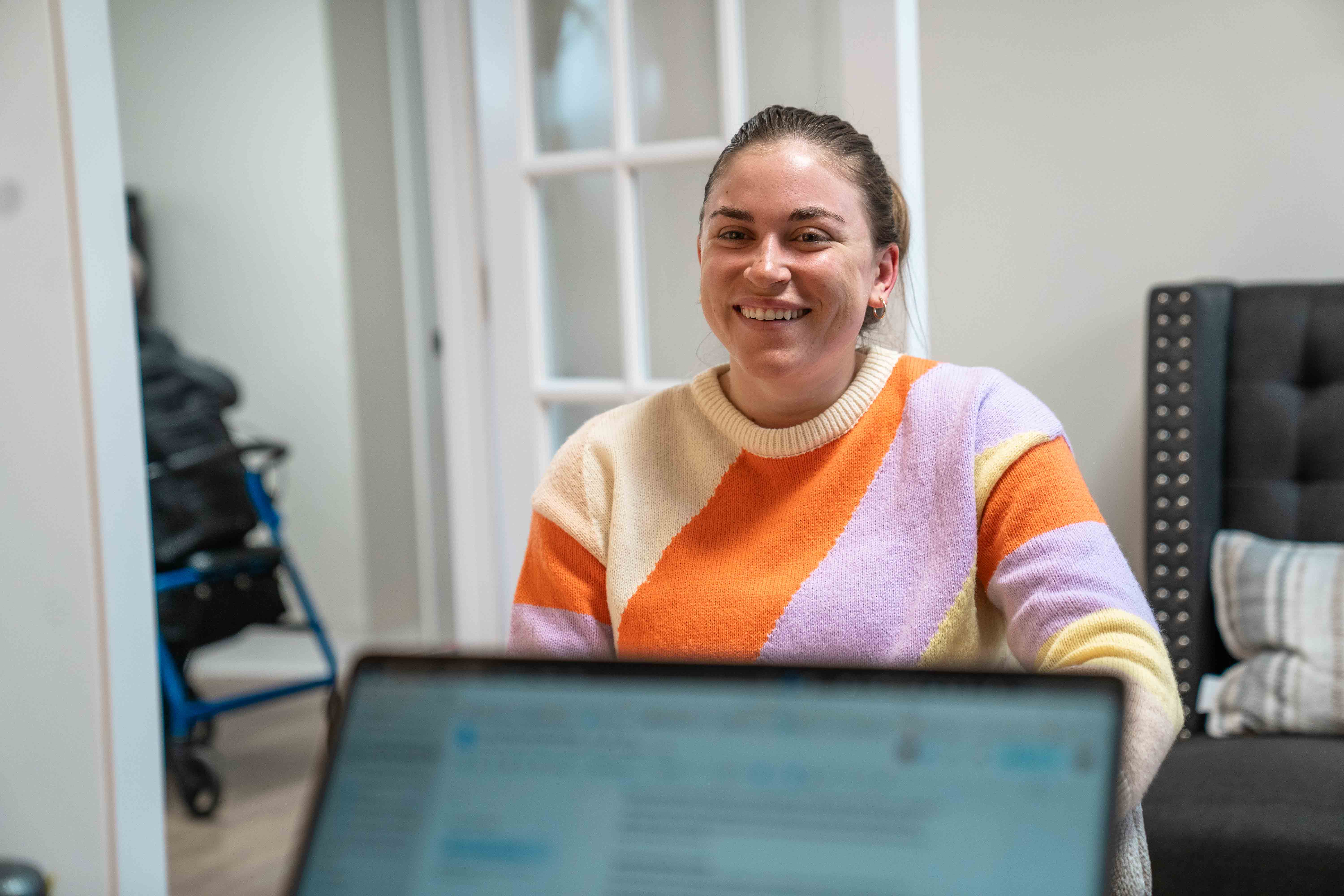 Woman sitting with laptop in hospital, church, or religious organization setting smiling at screen.