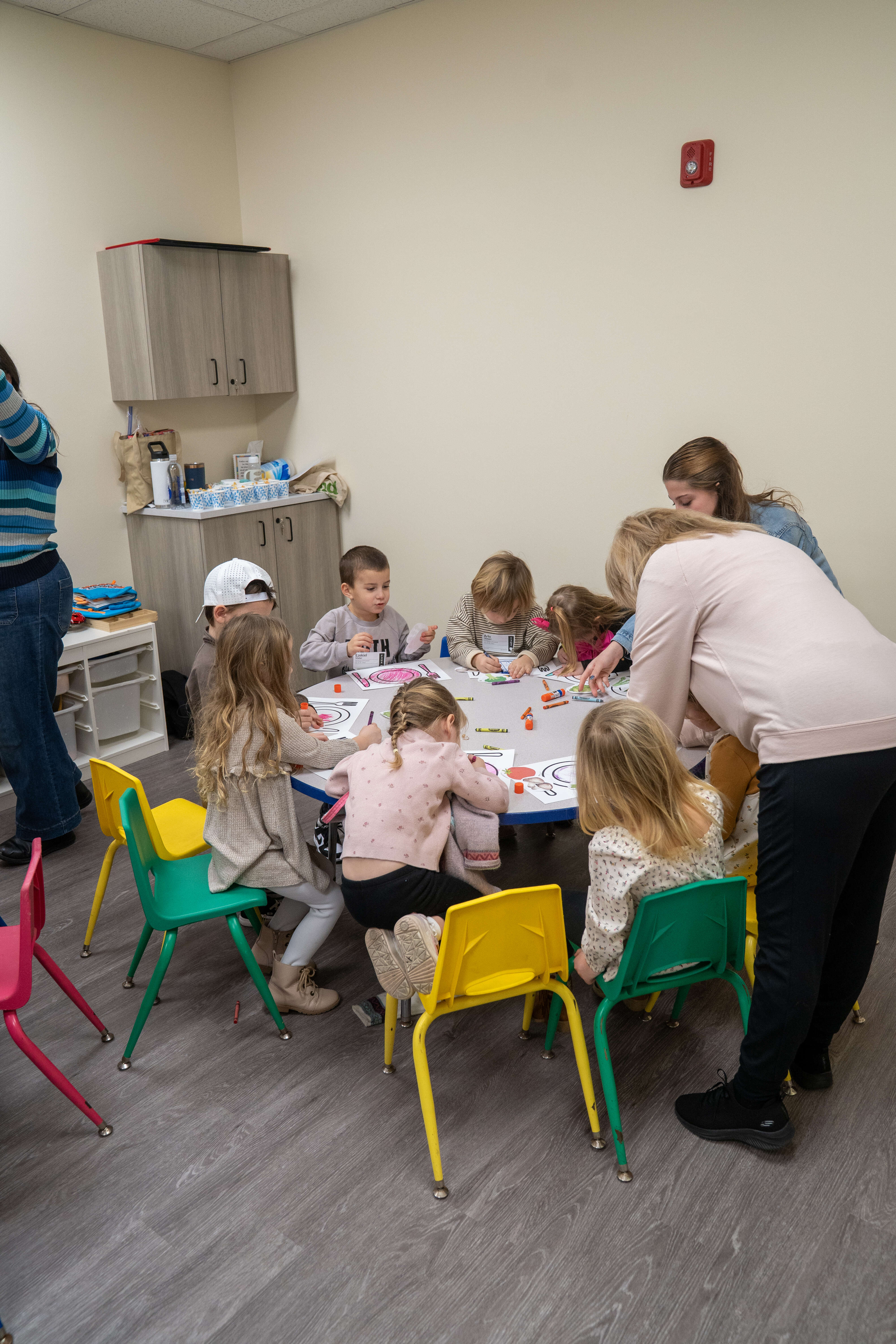 Children and adults coloring at a table in a church or hospital activity room together.