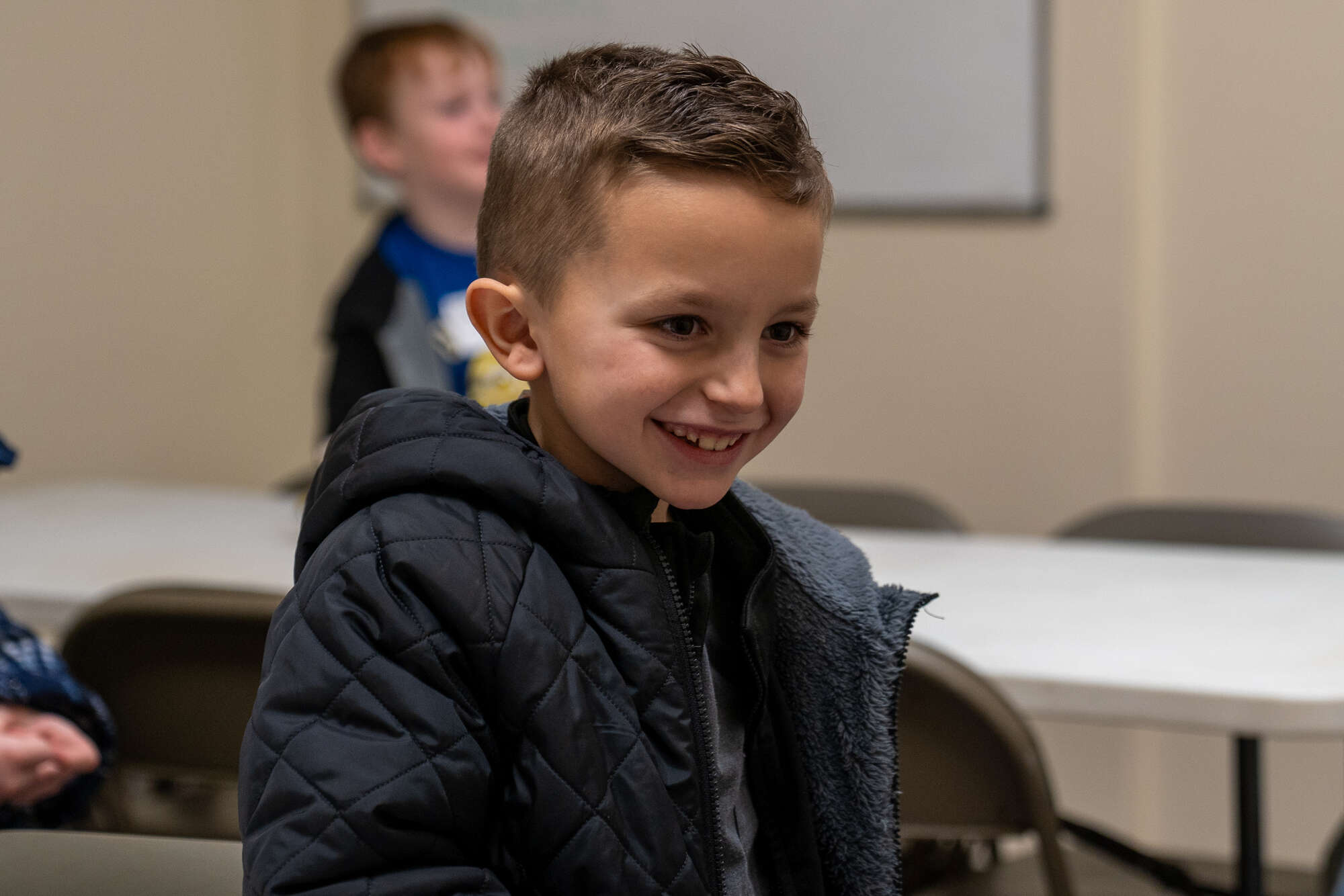 Young boy smiling at church or hospital event, wearing a black puffer jacket.