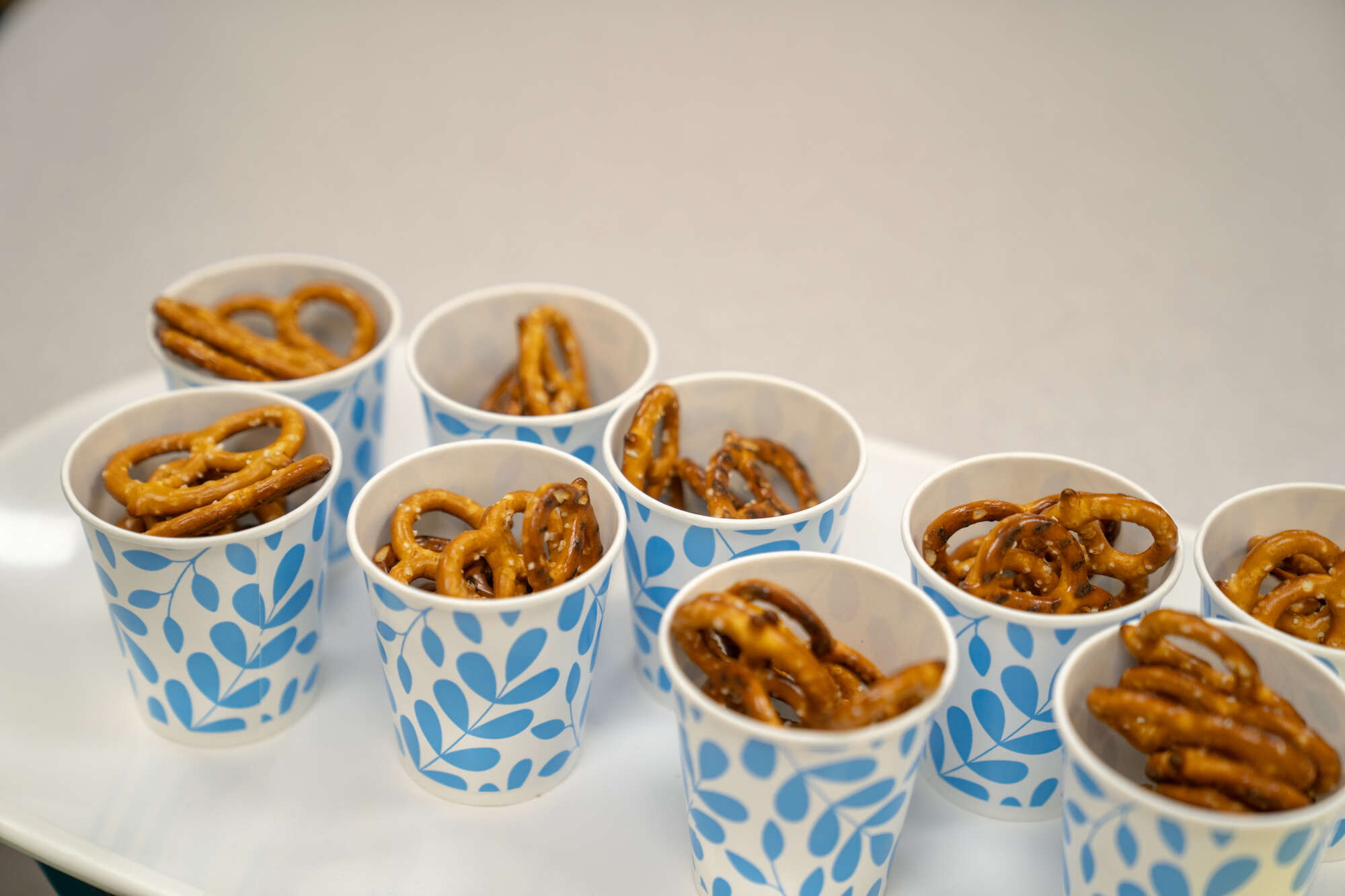 Pretzels in blue and white patterned paper cups on white tray at church event or hospital.