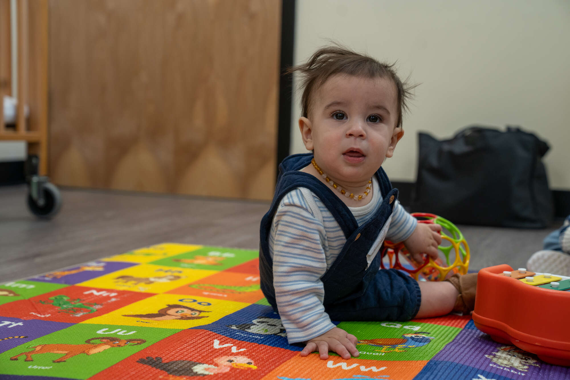 Baby sitting on colorful alphabet playmat in hospital or church nursery with toy.