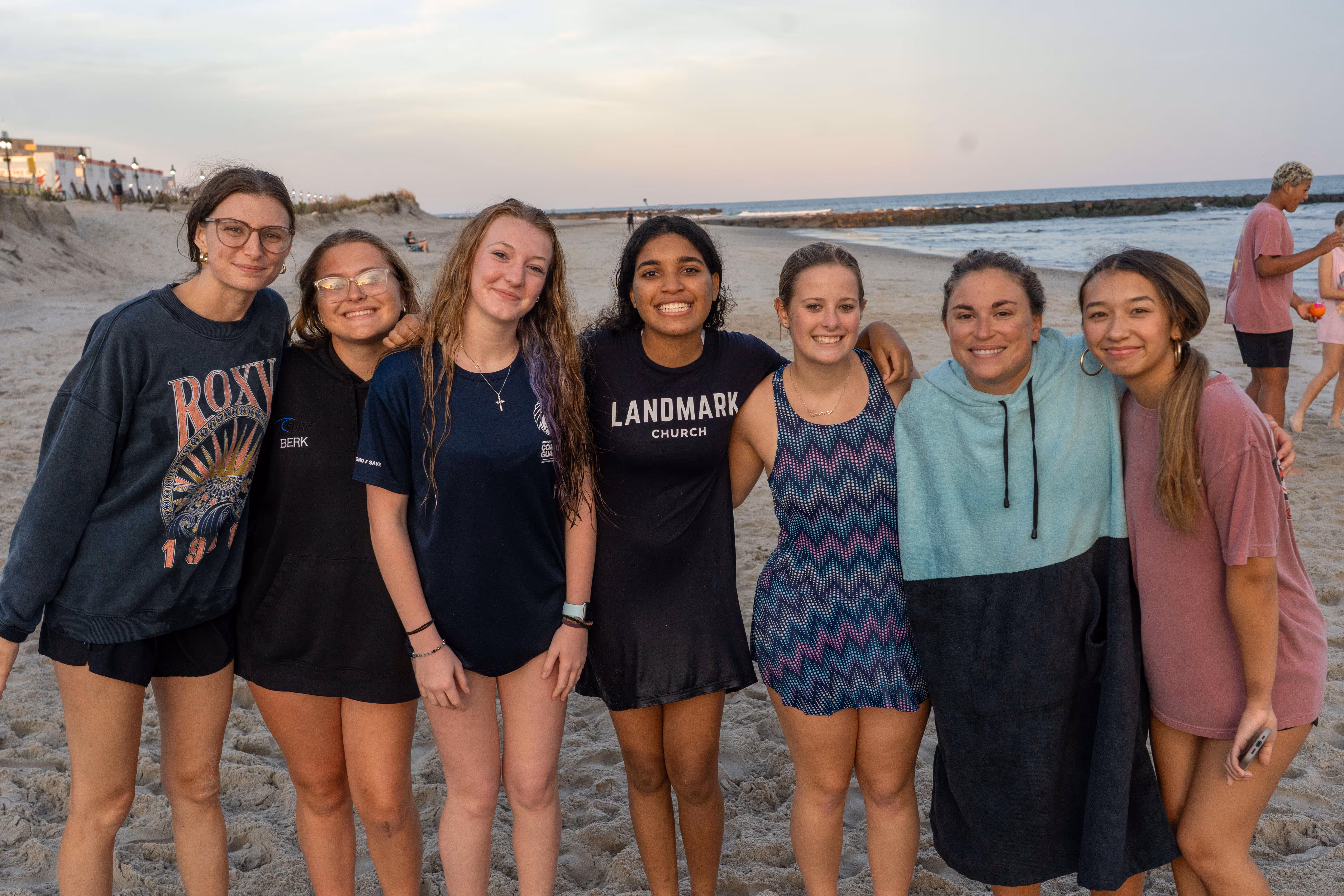 Young women from Landmark Church posing together on a beach near a hospital or religious event.