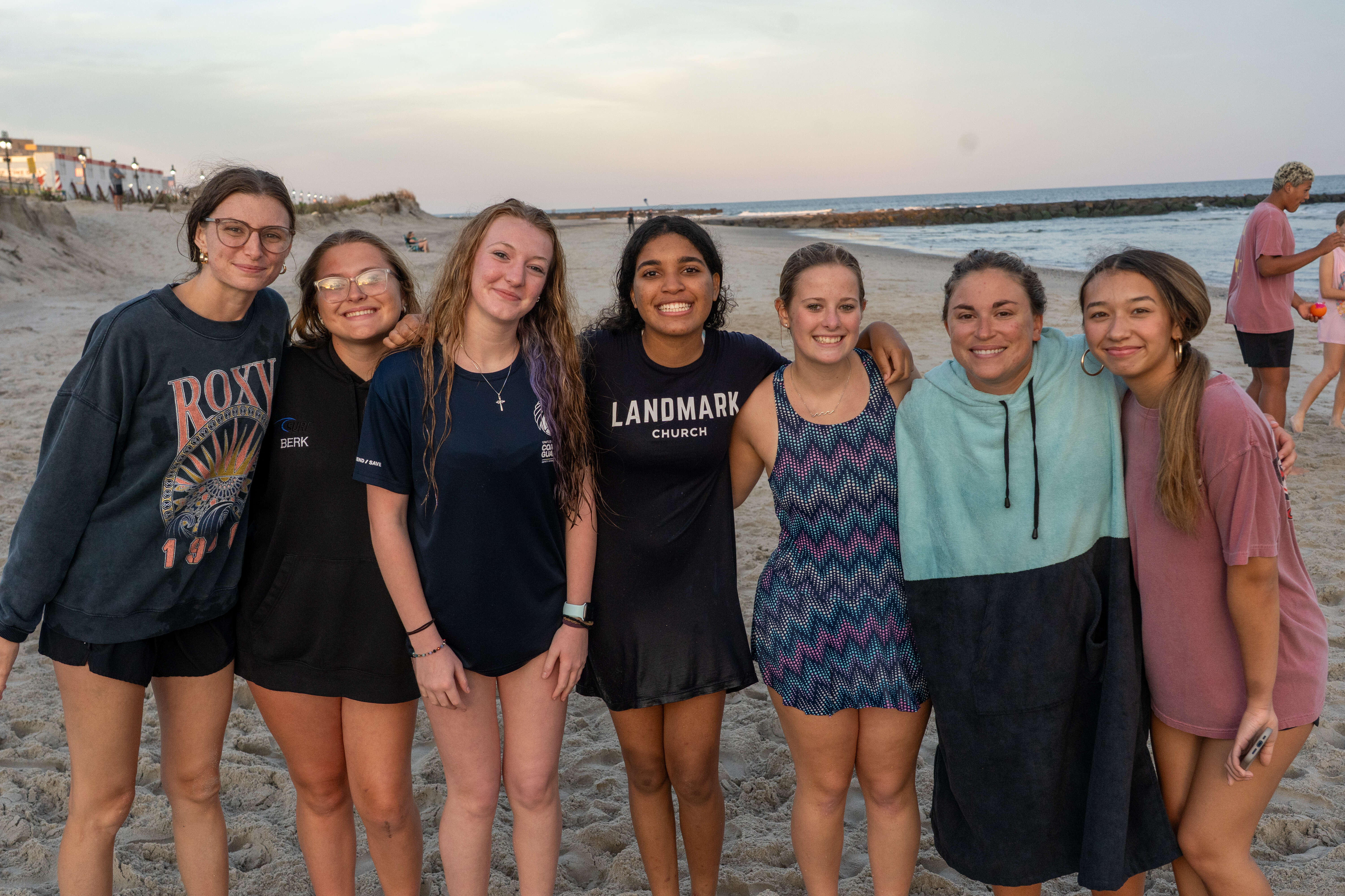 Young women from Landmark Church posing together on a beach near a hospital or religious event.