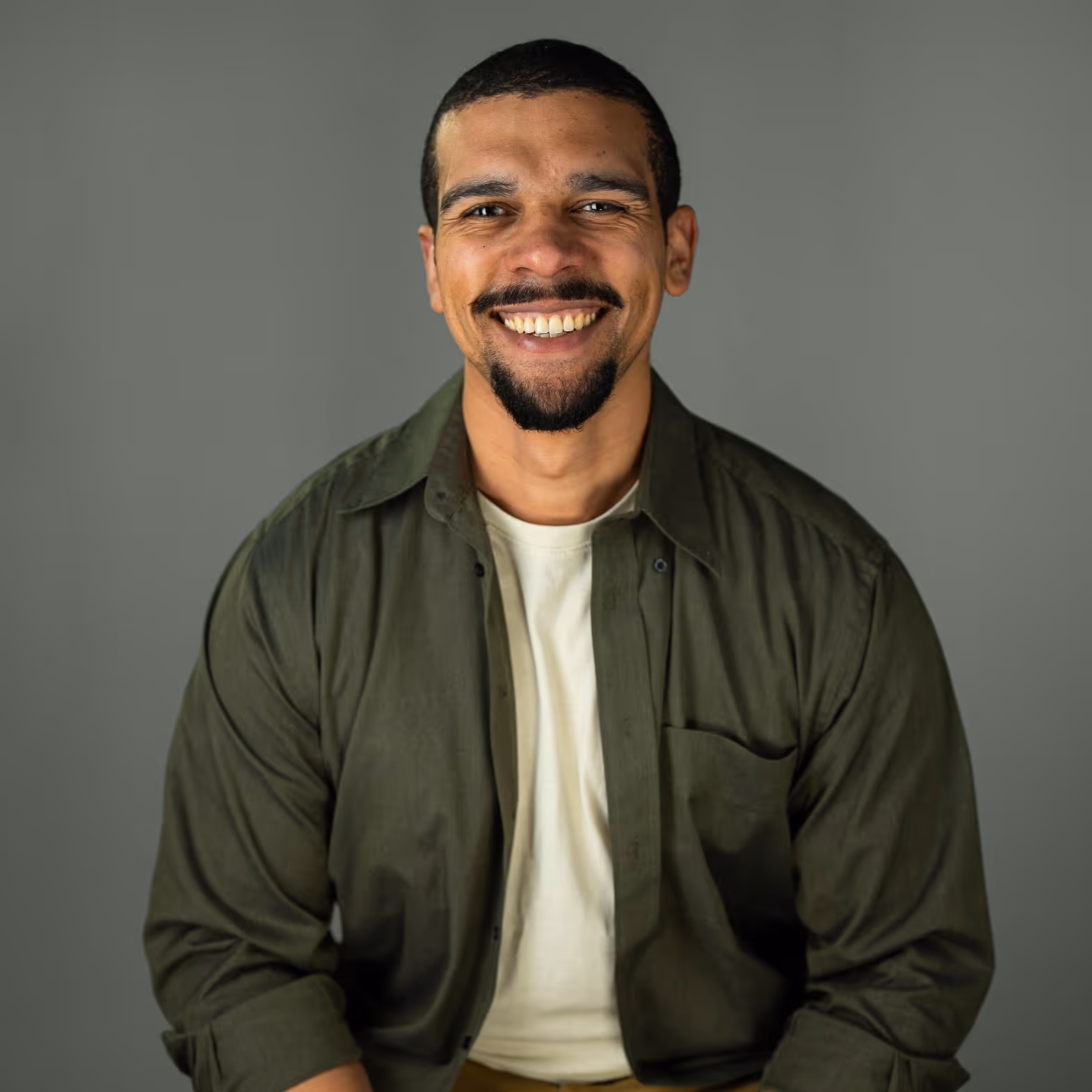 Smiling man in green shirt and white t-shirt against gray background, church or hospital staff.