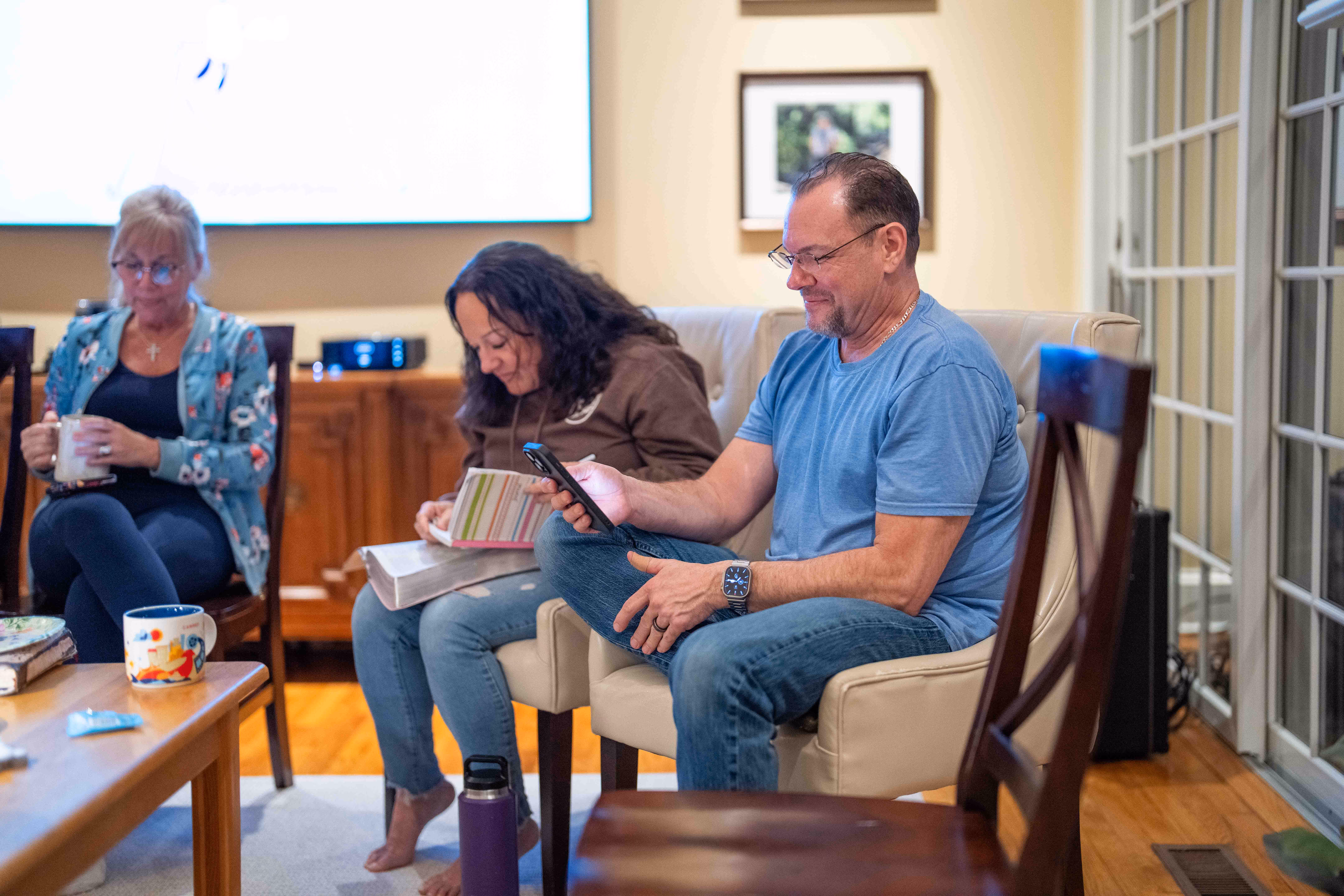 People sitting in living room with book and phone at church or hospital gathering.