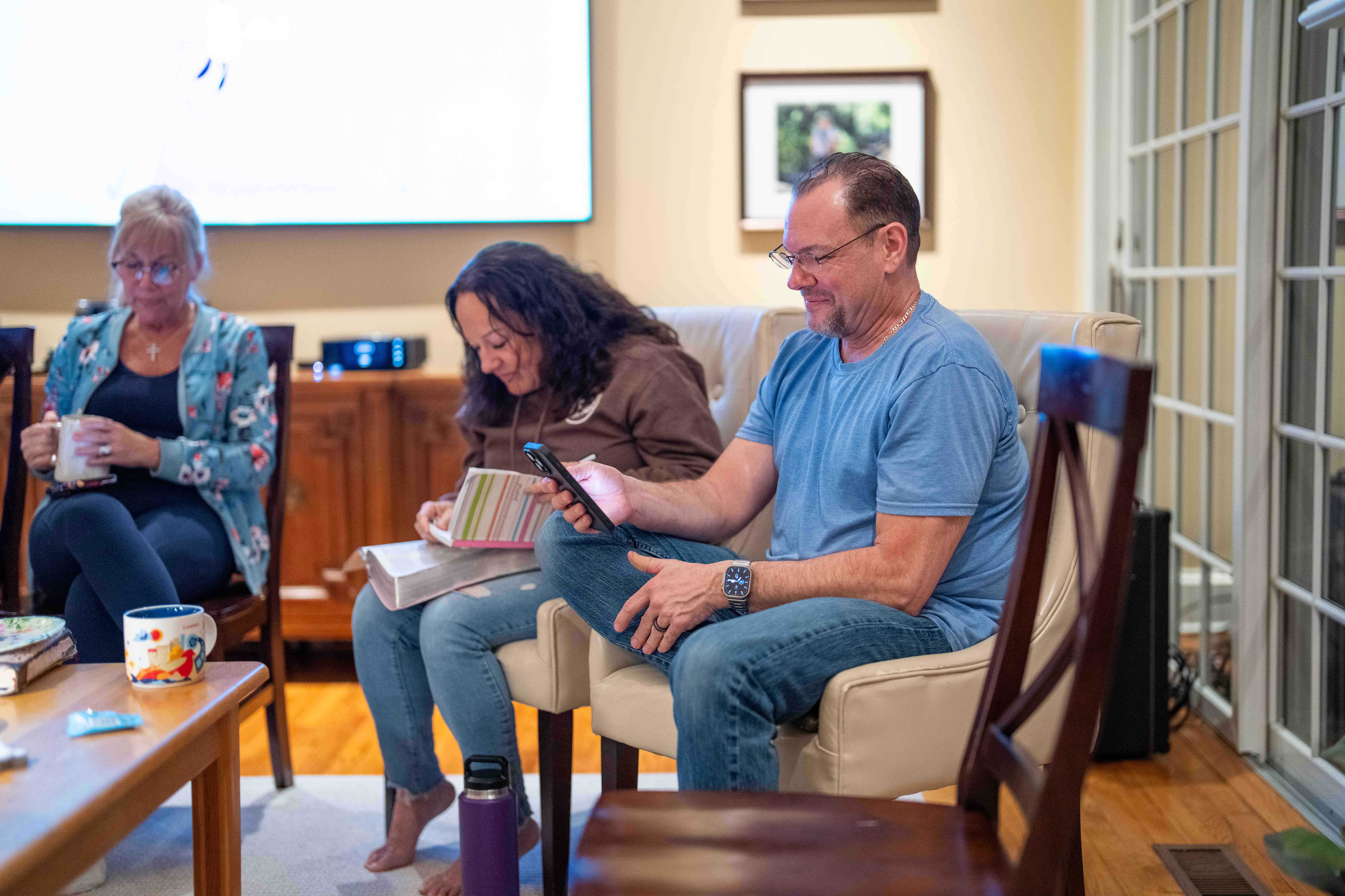 People sitting in living room with book and phone at church or hospital gathering.