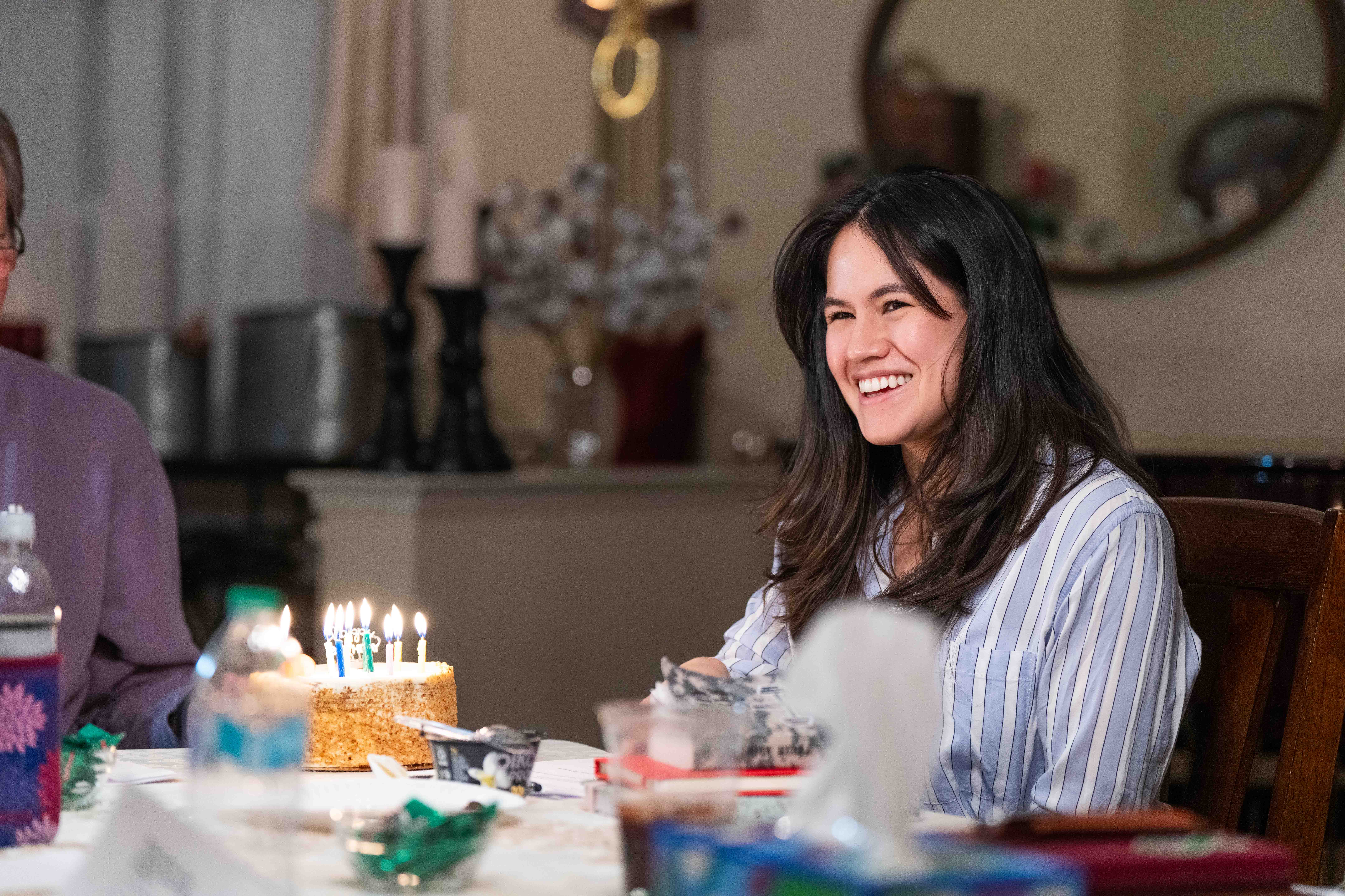 Woman sitting at table with birthday cake and candles in church or hospital setting celebration.