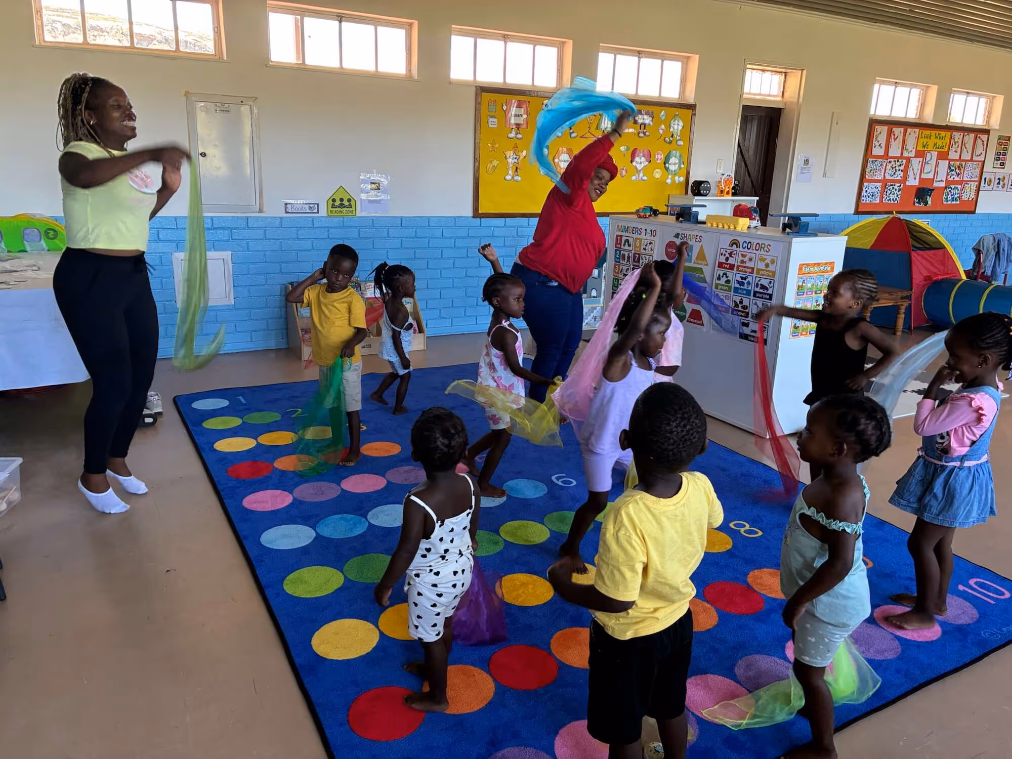 Children play with colorful scarves in a classroom setting at a church or hospital nursery.