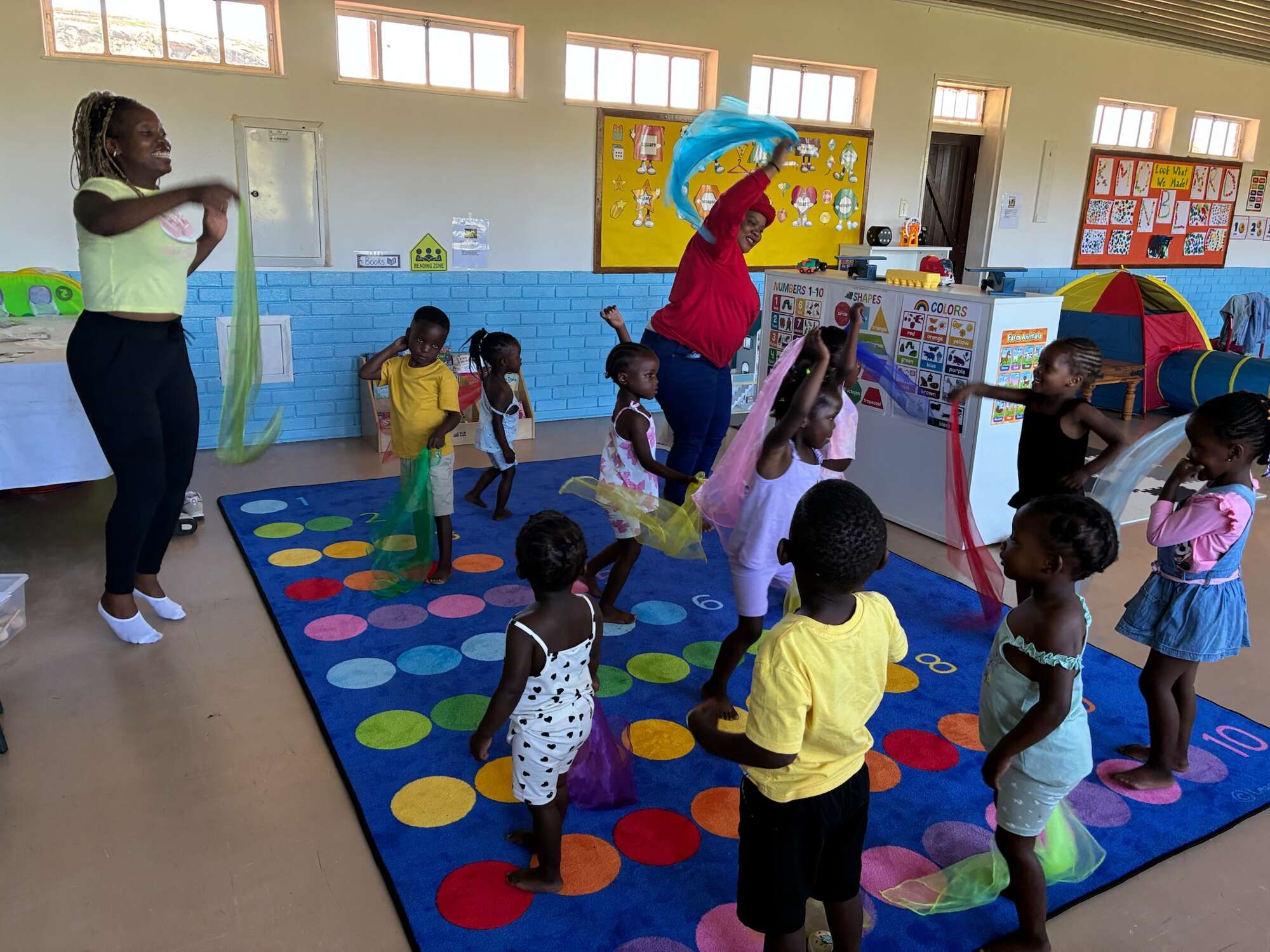 Children play with colorful scarves in a classroom setting at a church or hospital nursery.