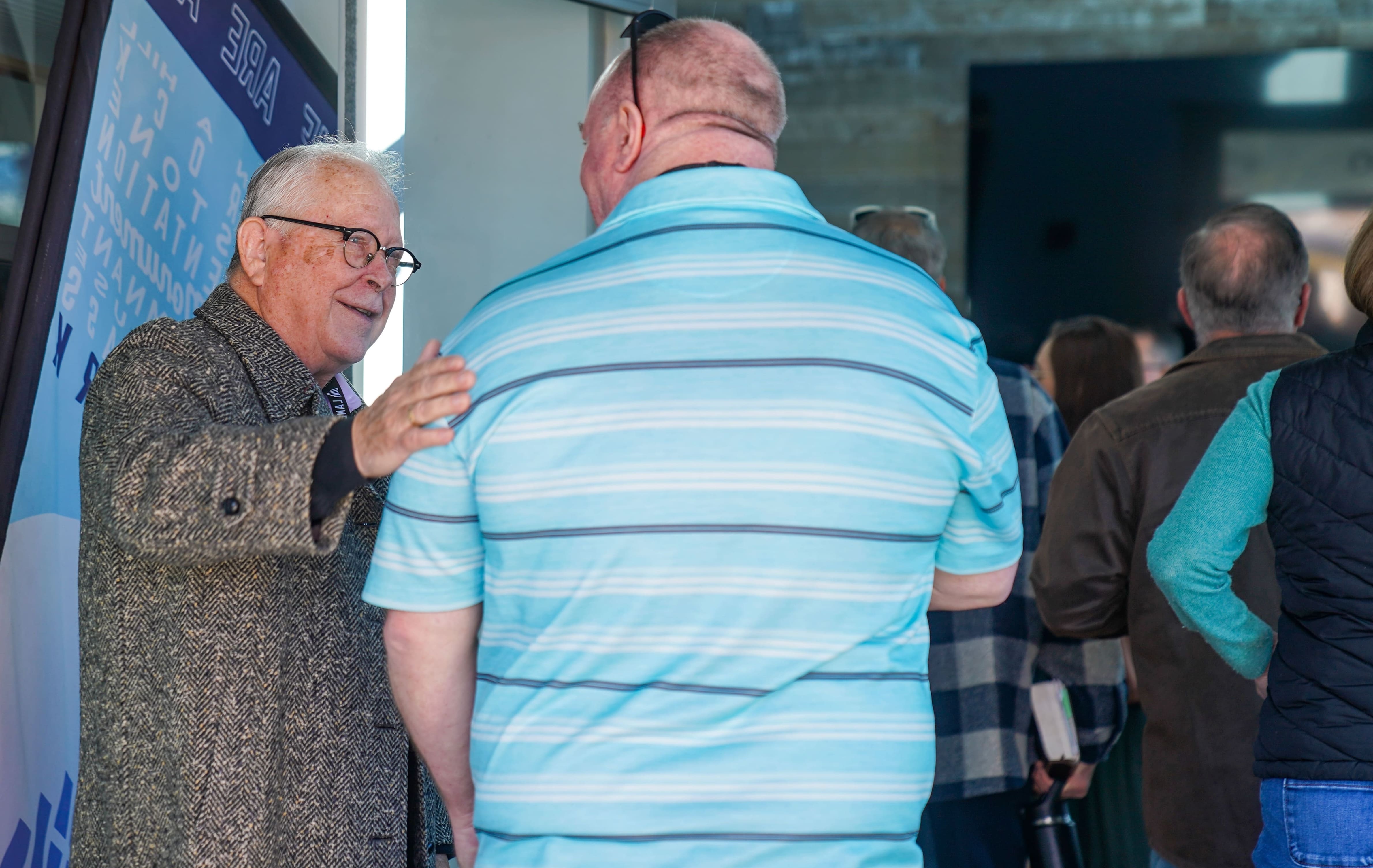 Elderly man talking to another man at a church or hospital community event gathering.