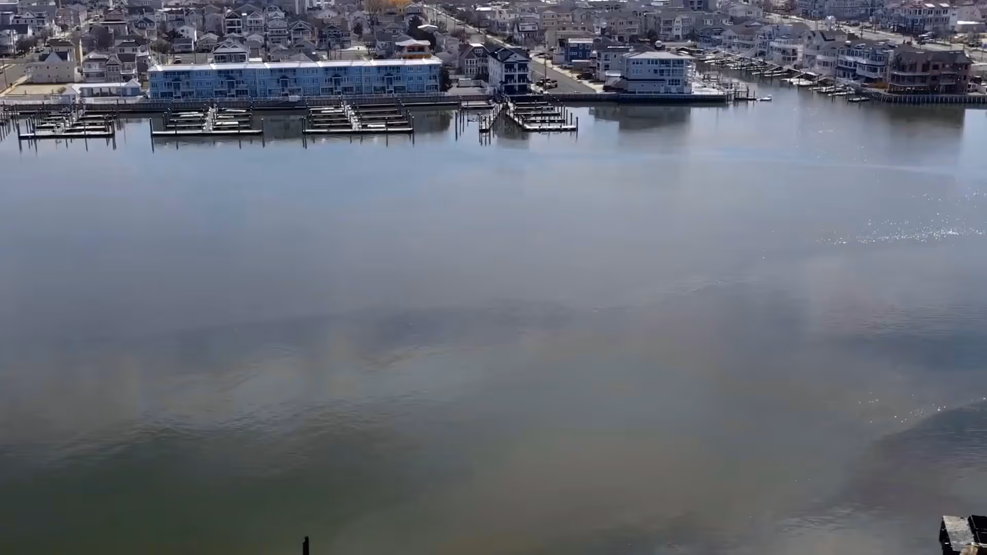 Waterfront view of docks and houses lining a calm bay under daylight.