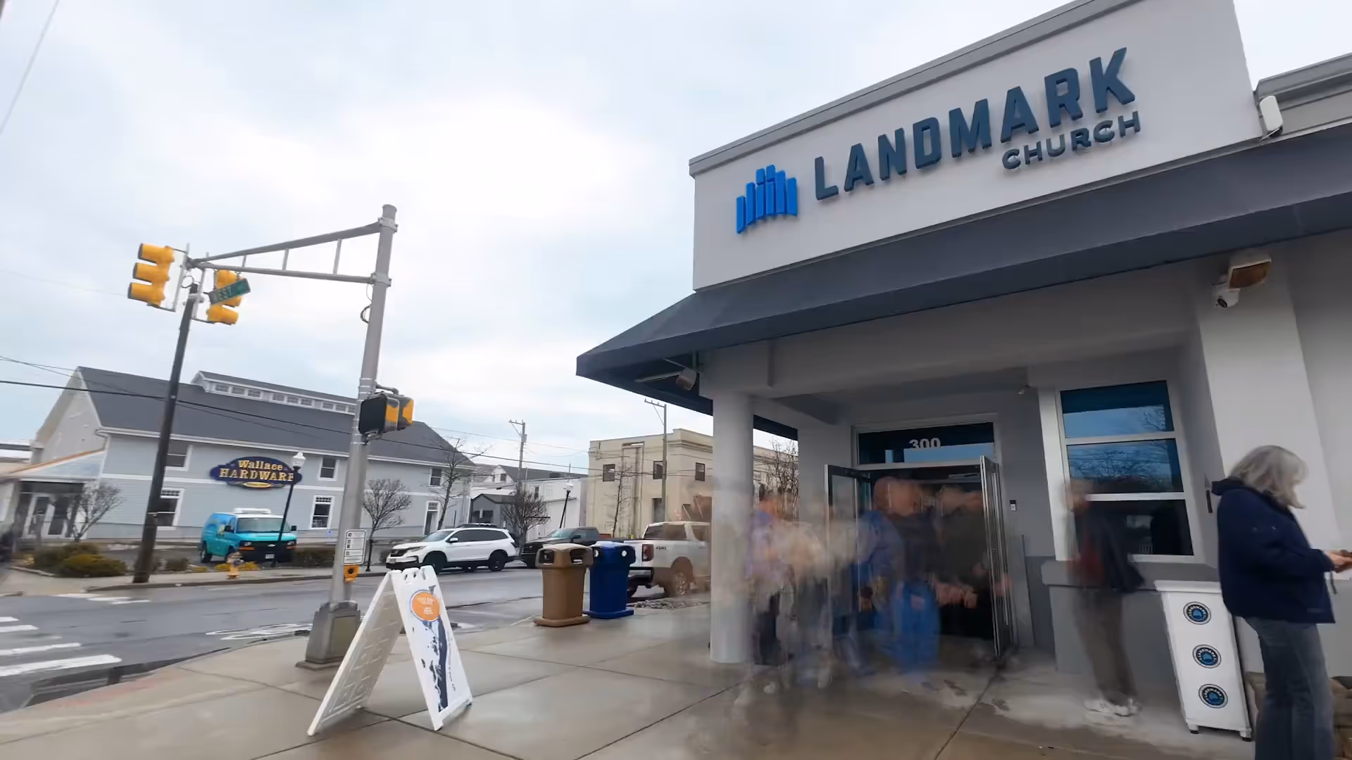 People entering Landmark Church with a hardware store visible across the street on a cloudy day.
