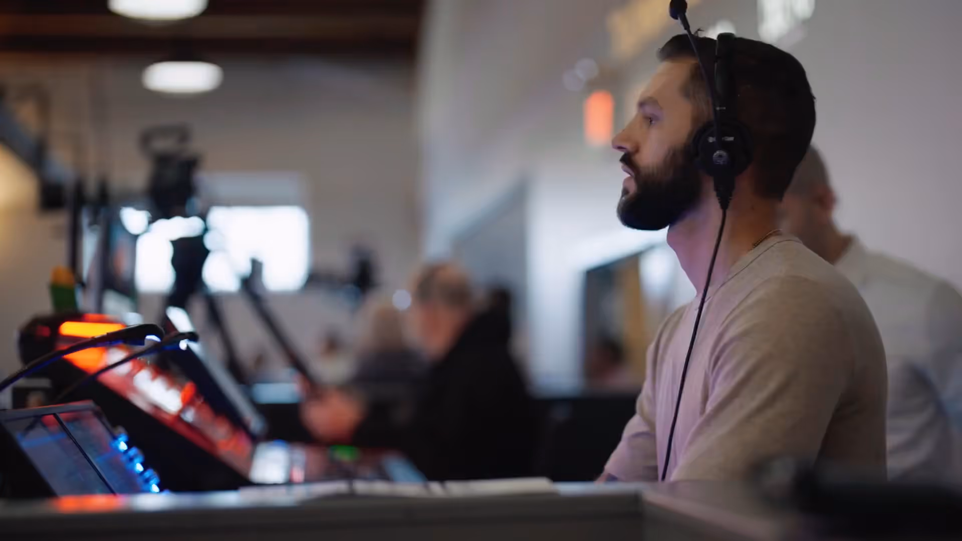Bearded man wearing headphones working with audio or lighting control board in a studio.