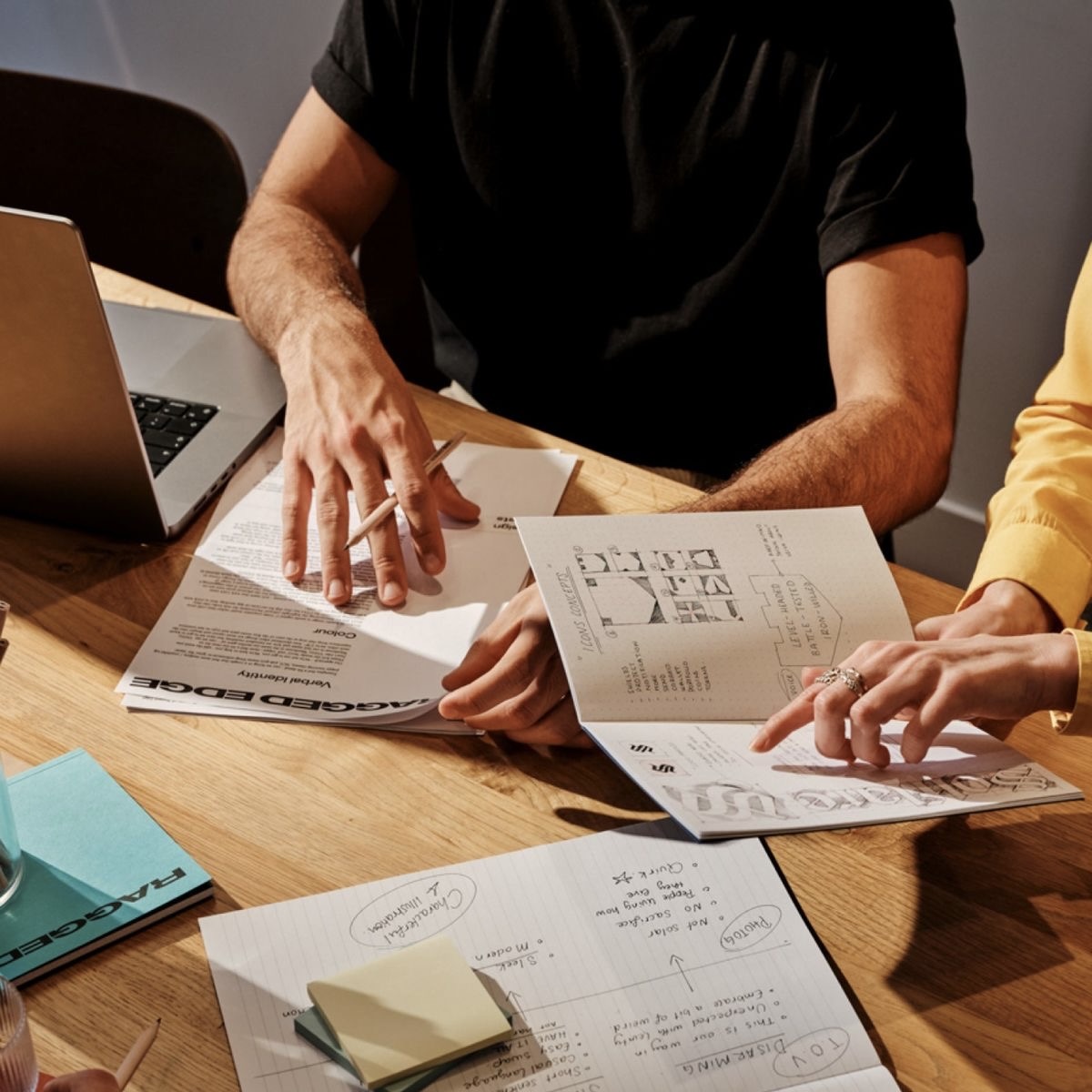 People collaborating at a wooden table with documents, a laptop, and notes scattered around.
