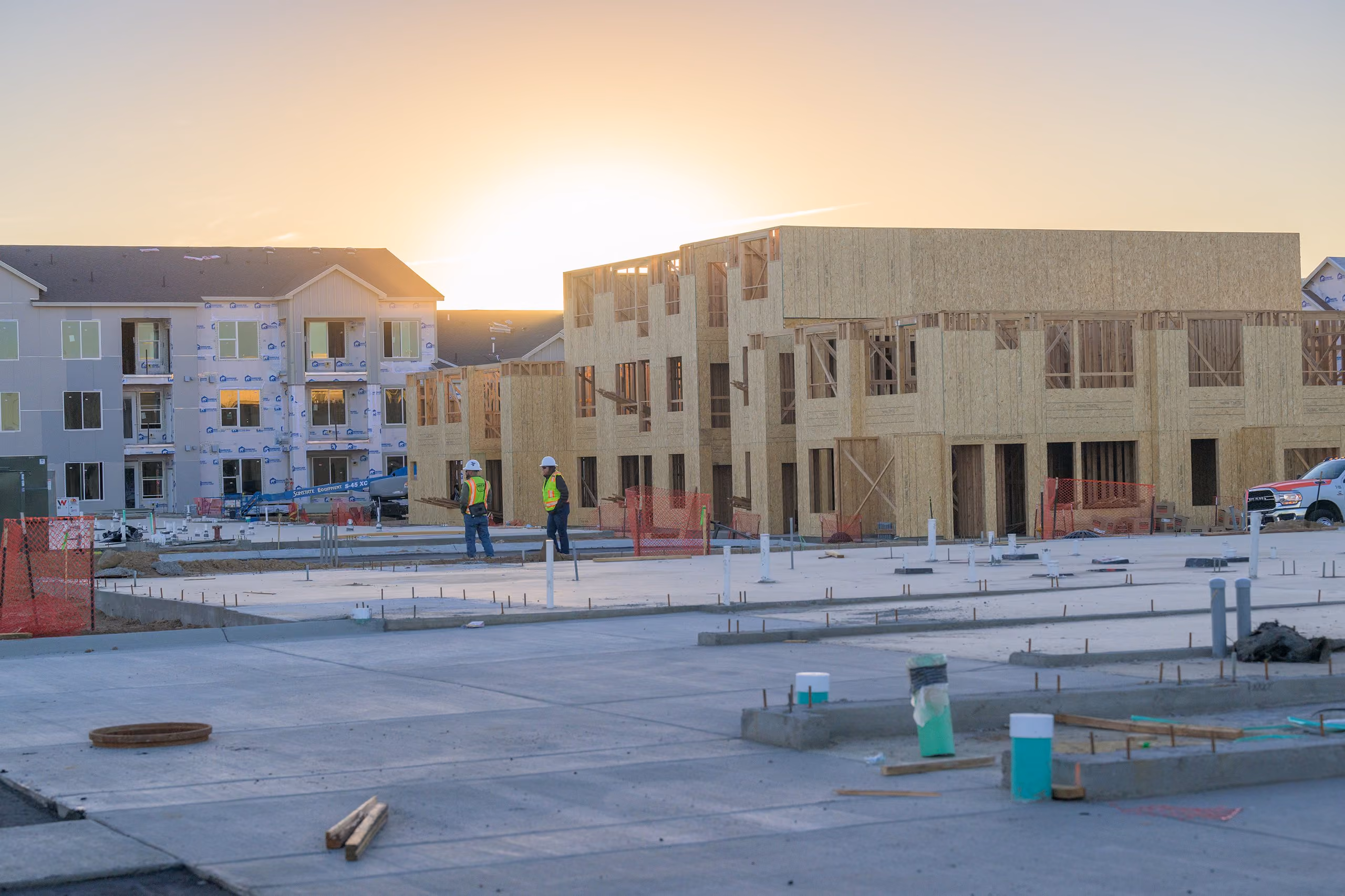 Multi-family apartment buildings under construction with a freshly poured concrete courtyard, illustrating the New Construction Contractors industry card in the homepage's "Who we serve" section