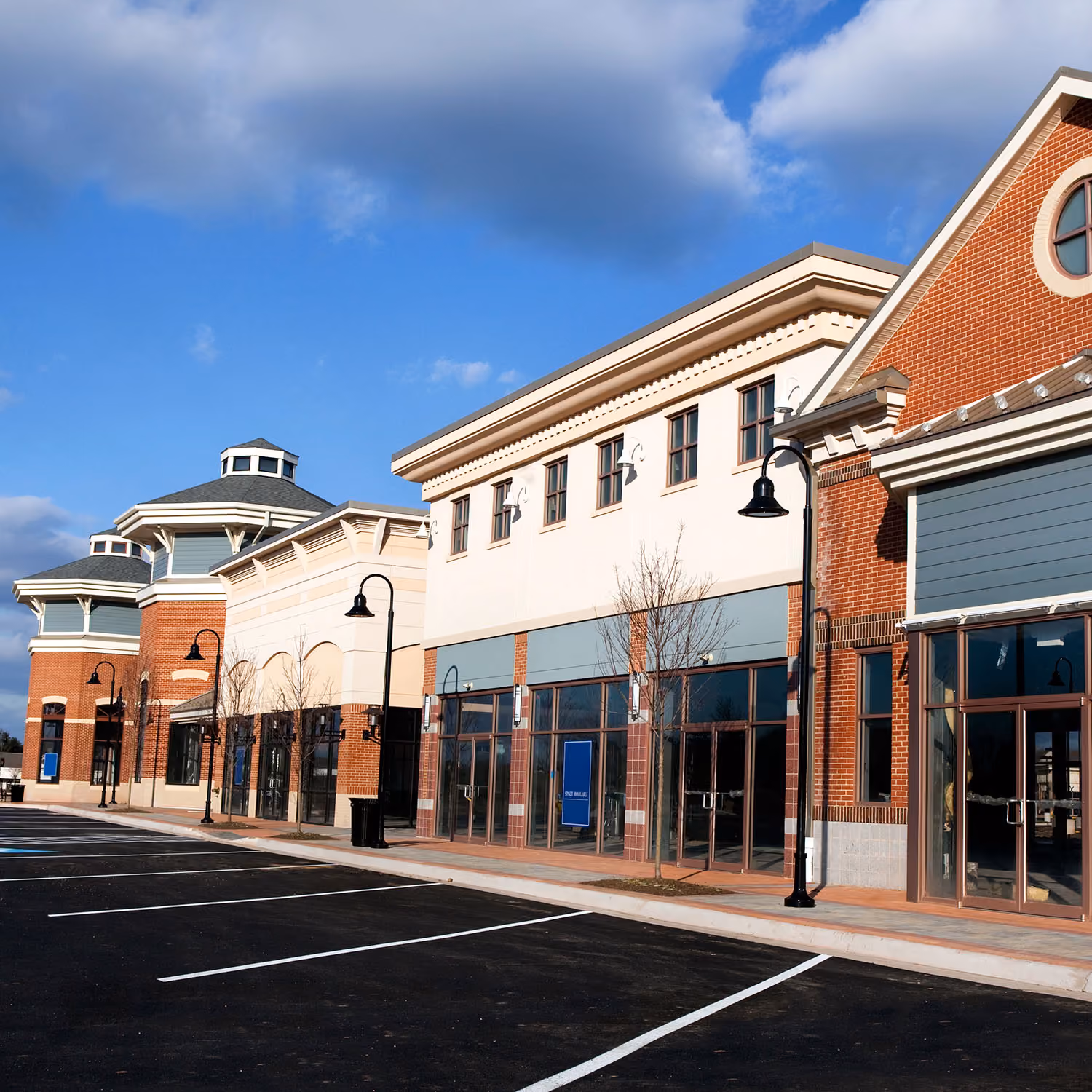 Brick-and-stone retail shopping center storefronts with a freshly striped, empty parking lot, illustrating the Retail industry card in the homepage's "Who we serve" section
