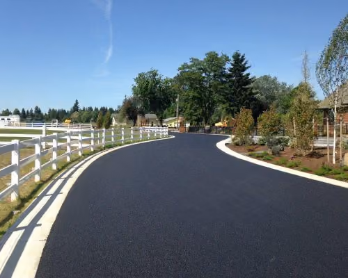 Newly paved, freshly striped road curving past white ranch-style fencing, illustrating the Municipal & Public Works industry card in the homepage's "Who we serve" section