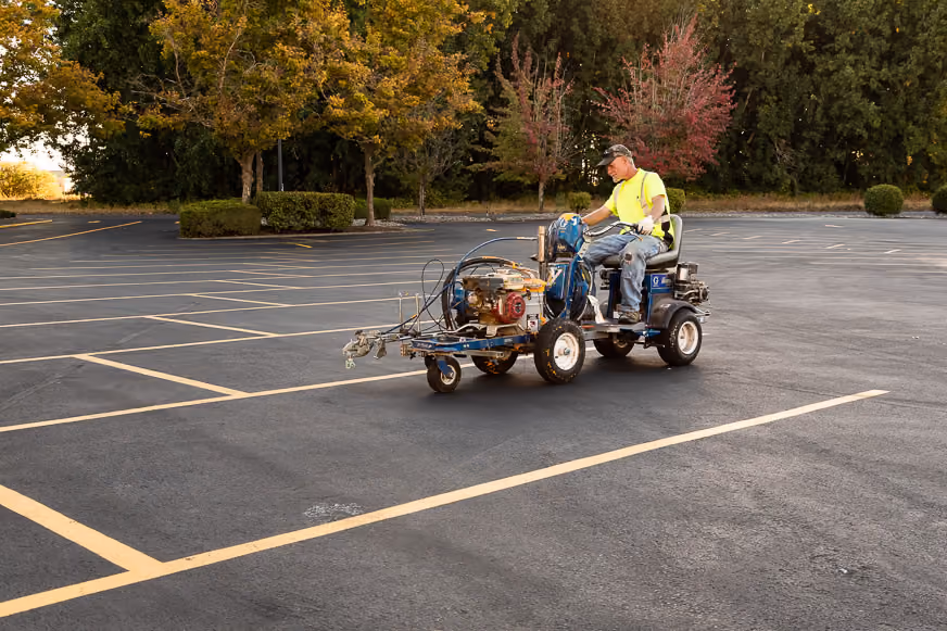 PMI Paving crew member riding a line-striping machine, painting fresh yellow parking stall lines