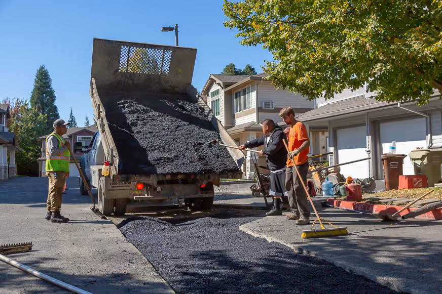 PMI Paving crew raking fresh asphalt from a dump truck onto a residential street