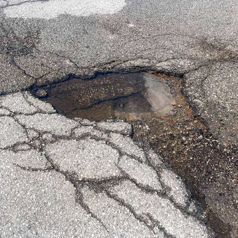 Close-up of a deteriorated asphalt surface with a large water-filled pothole and alligator cracking