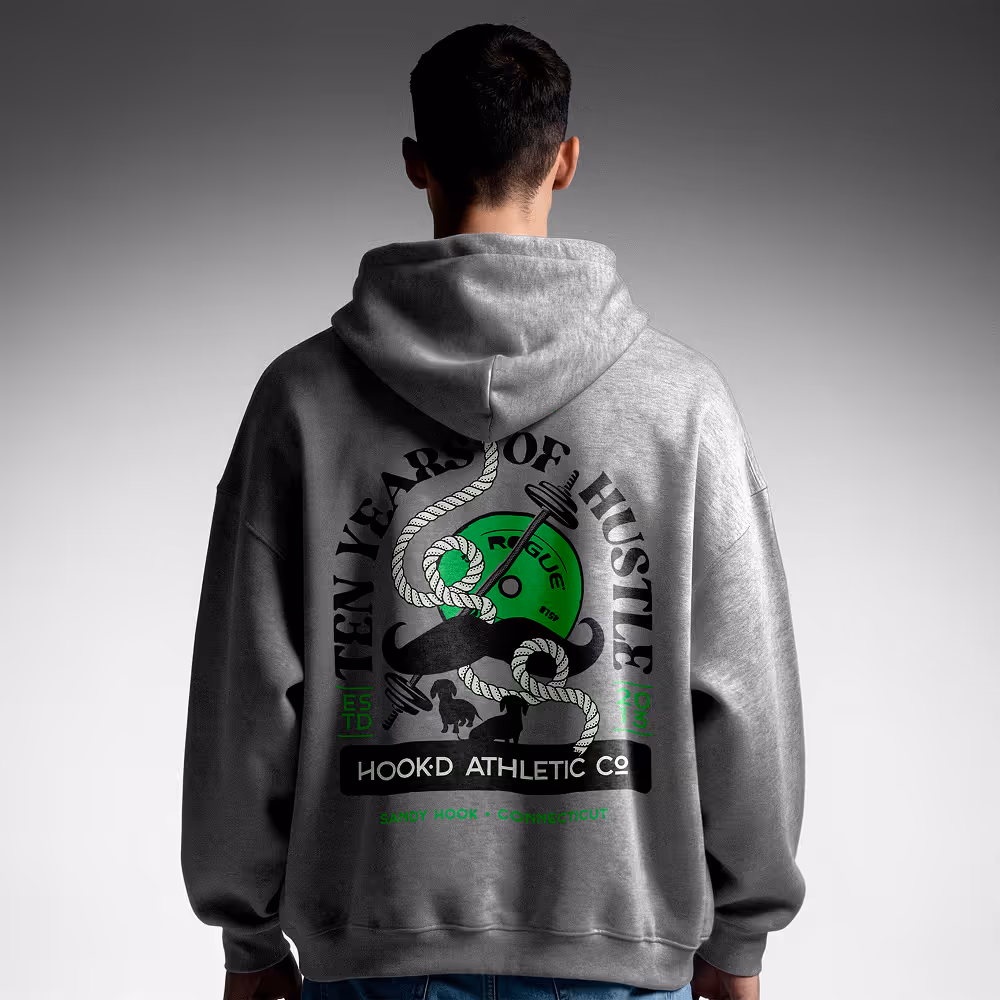 Person seen from the back wearing a gray hoodie with a design featuring a green weight plate, rope, black mustache, and text reading 'Ten Years of Hustle' and 'Hook'd Athletic Co.'