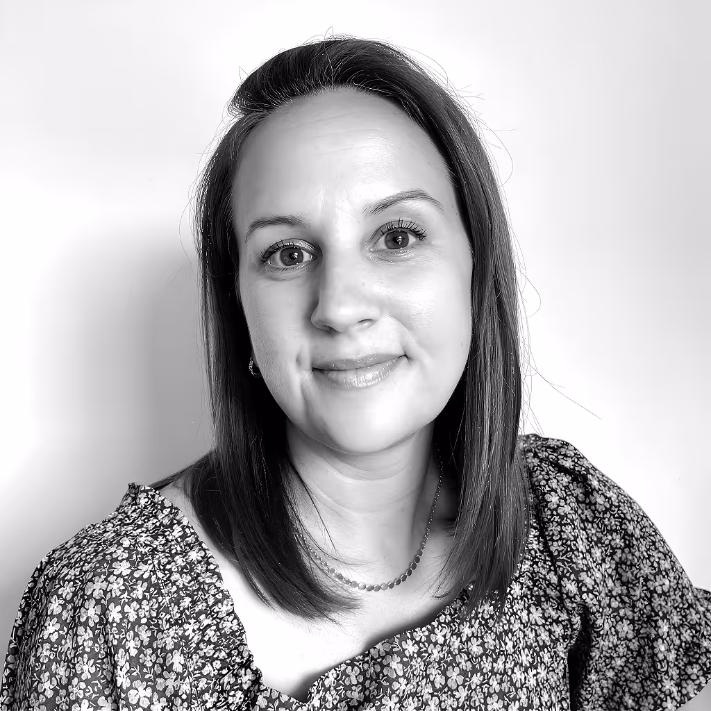 Smiling woman with straight shoulder-length hair wearing a floral patterned top and necklace, against a plain background.