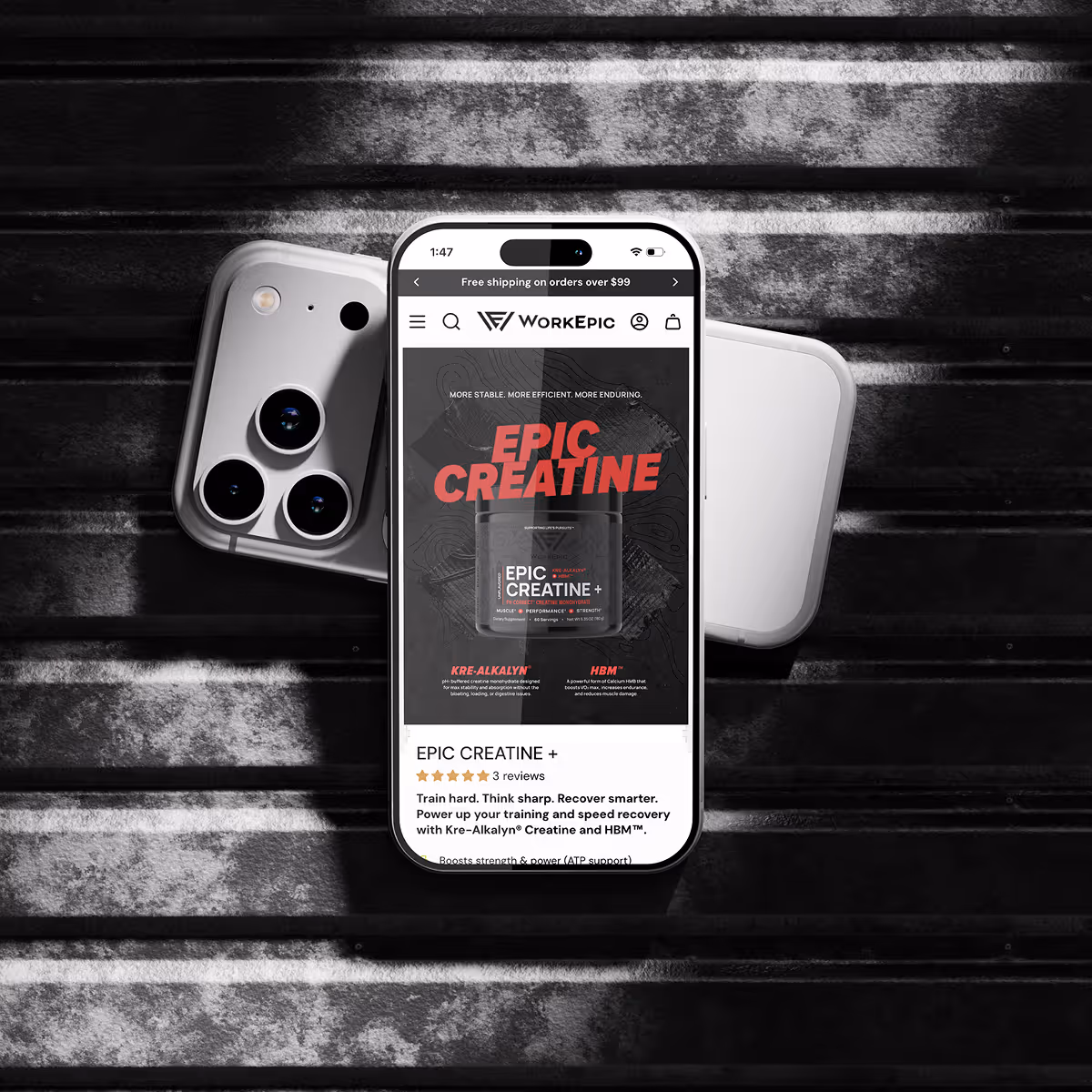 Smartphone displaying WorkEpic website featuring EPIC CREATINE + supplement, resting on silver and white smartphones on a dark striped surface.