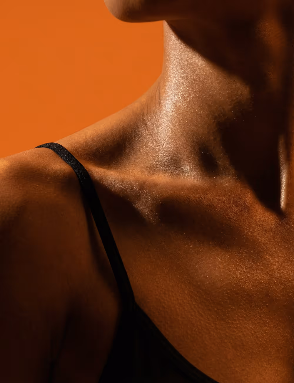 Close-up of a person's shoulder and neck with a black strap against an orange background.