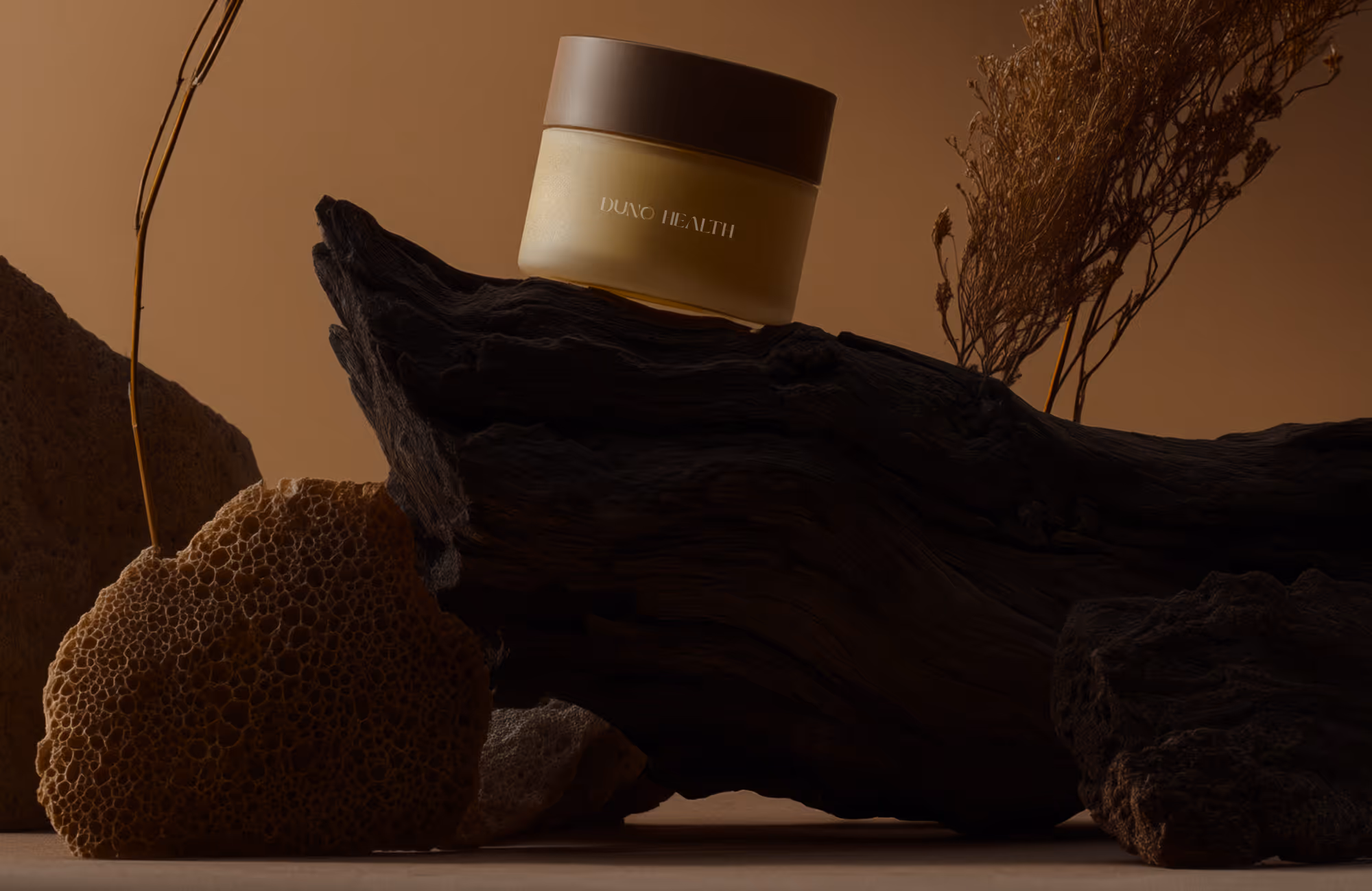 Duno Health cream jar on dark wood piece with natural sponges and dried plants on brown background.