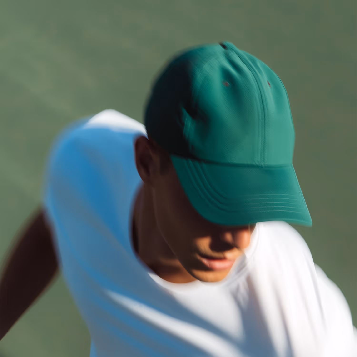 Young man wearing a green cap and white shirt looking downwards.