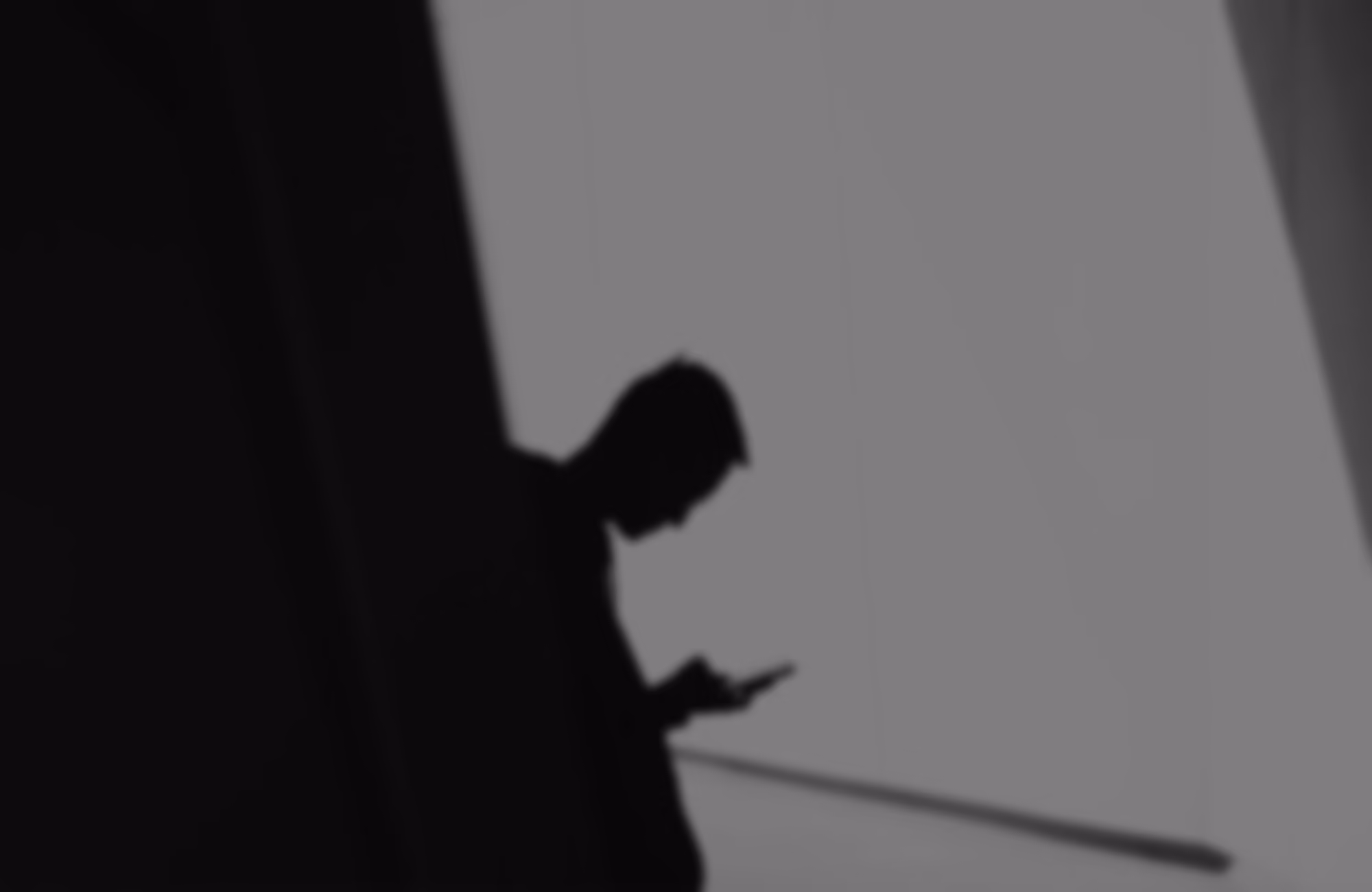 Silhouette of a person looking down at a mobile phone against a gray background, with parts of two vertical structures framing the sides.