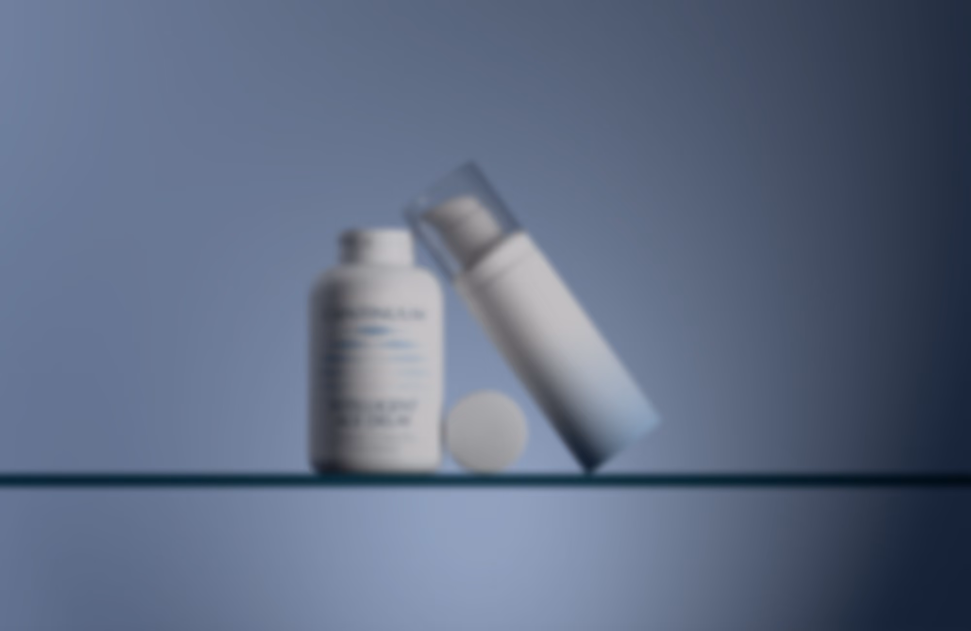 Two white cosmetic containers on a glass shelf against a blue background, one with a round cap removed placed nearby and one leaning with a transparent cap.
