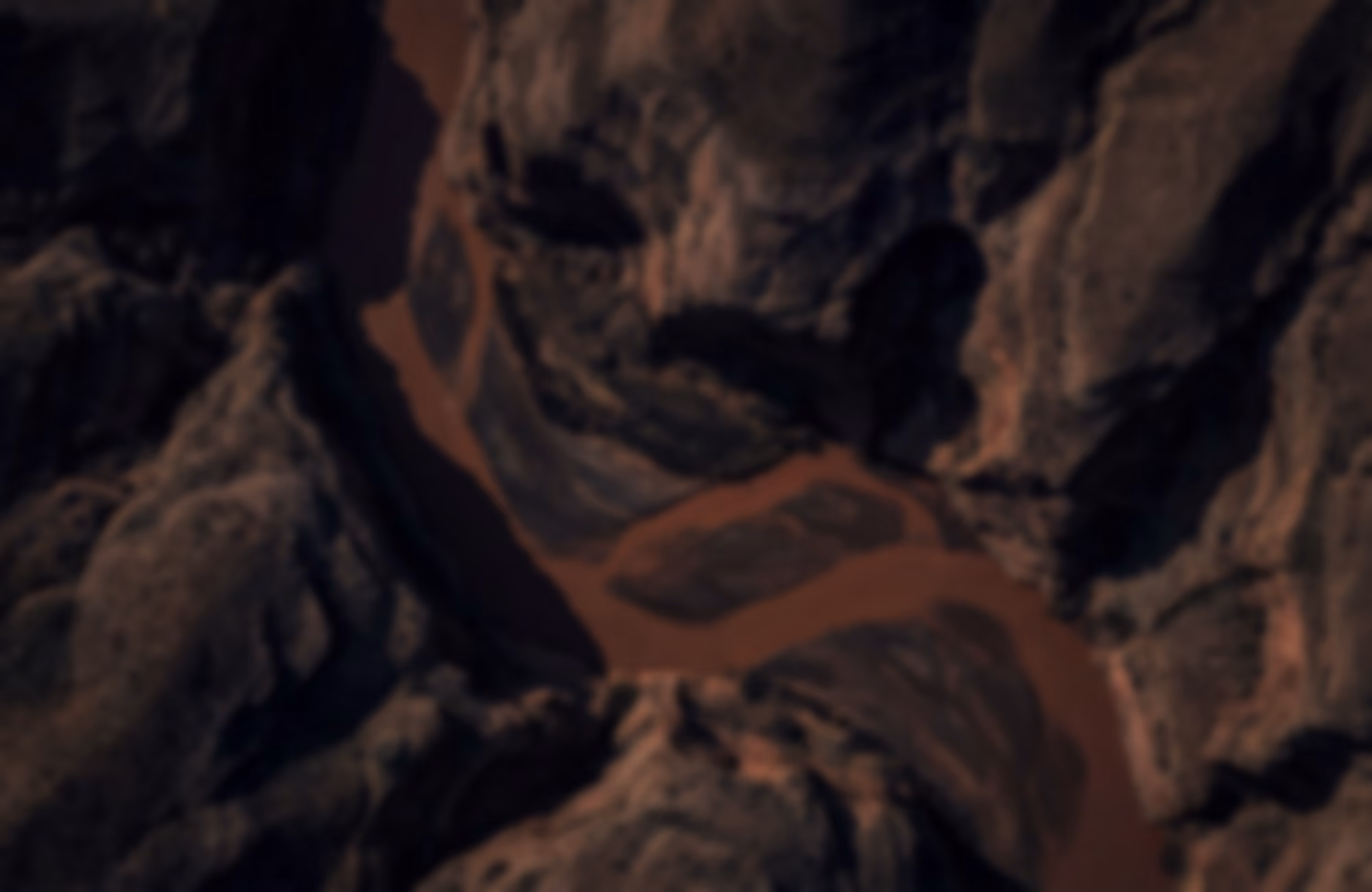 Aerial view of a winding reddish-brown river cutting through rugged, rocky terrain with steep cliffs on both sides.