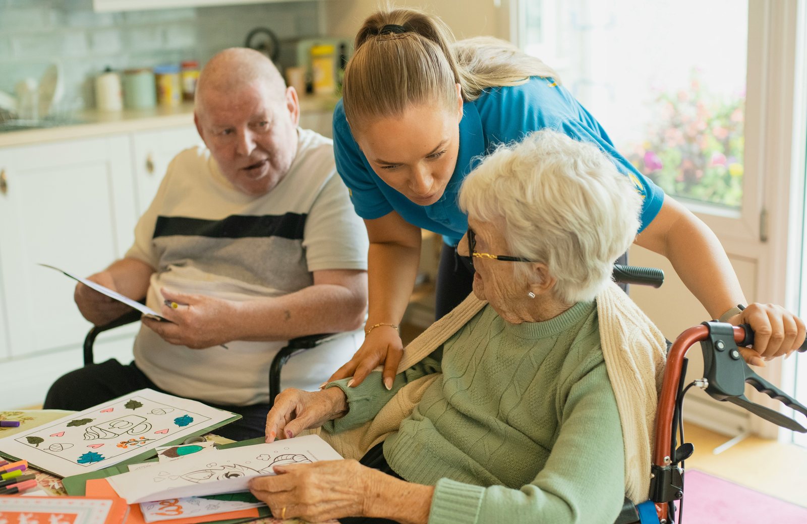 A carer helping two residents with an art activity