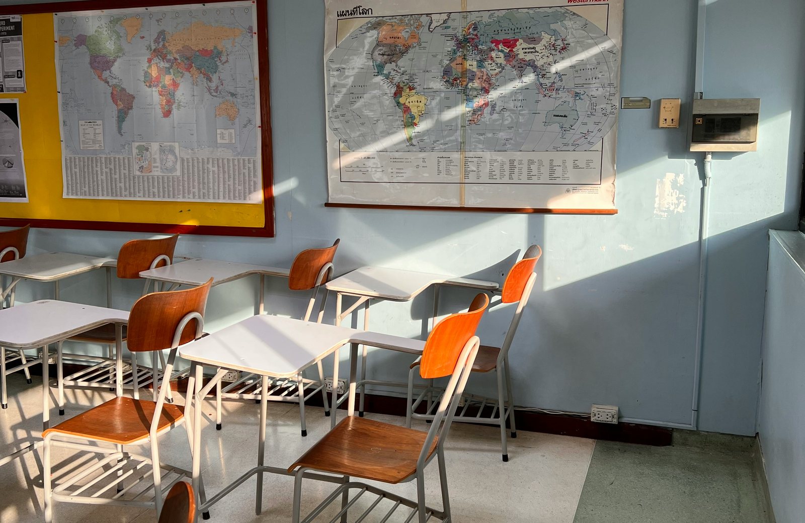 An empty sunlit classroom with desks and maps on the wall