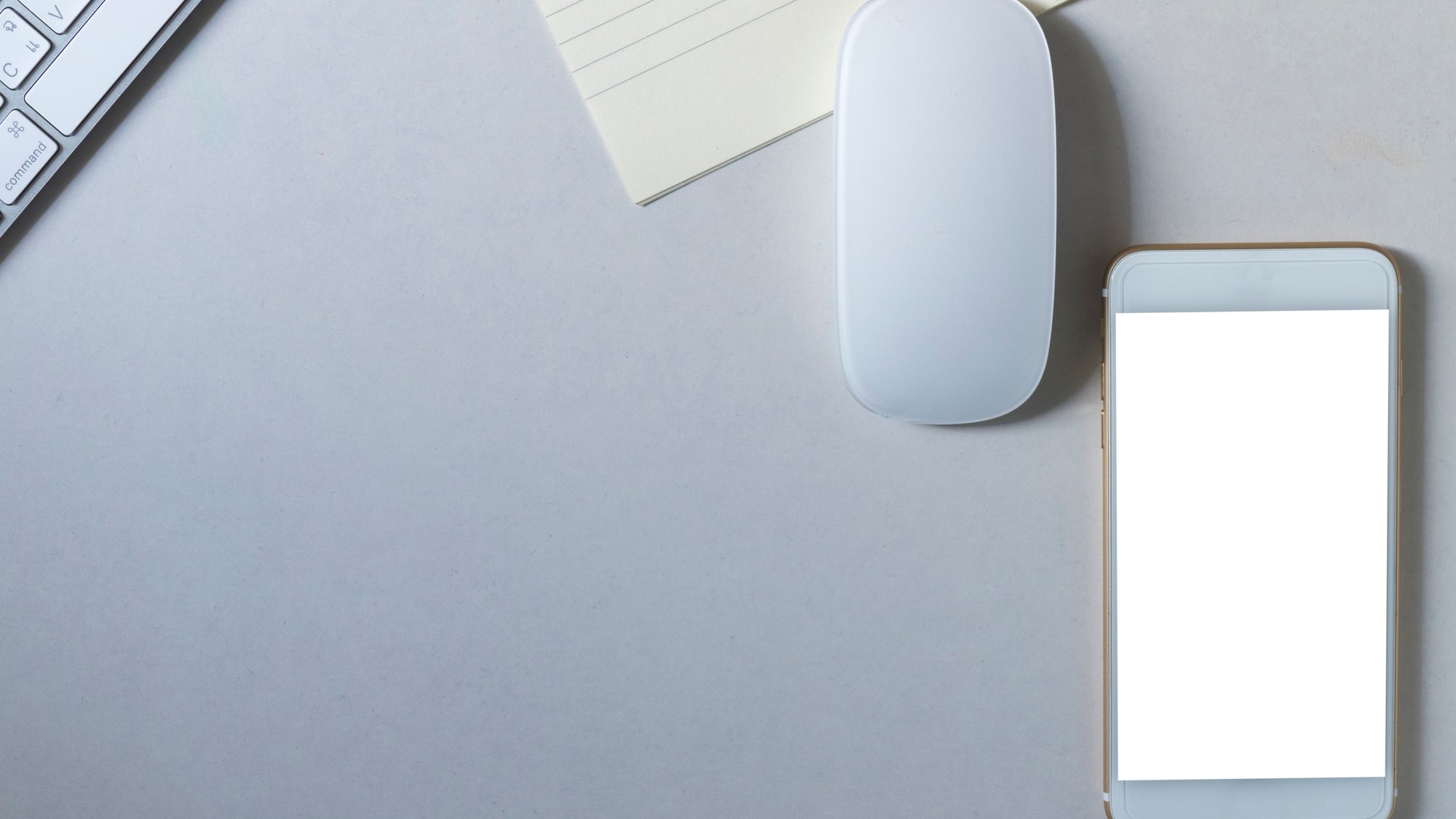 A phone, mouse and notepad on a desk, with the phone screen blank.