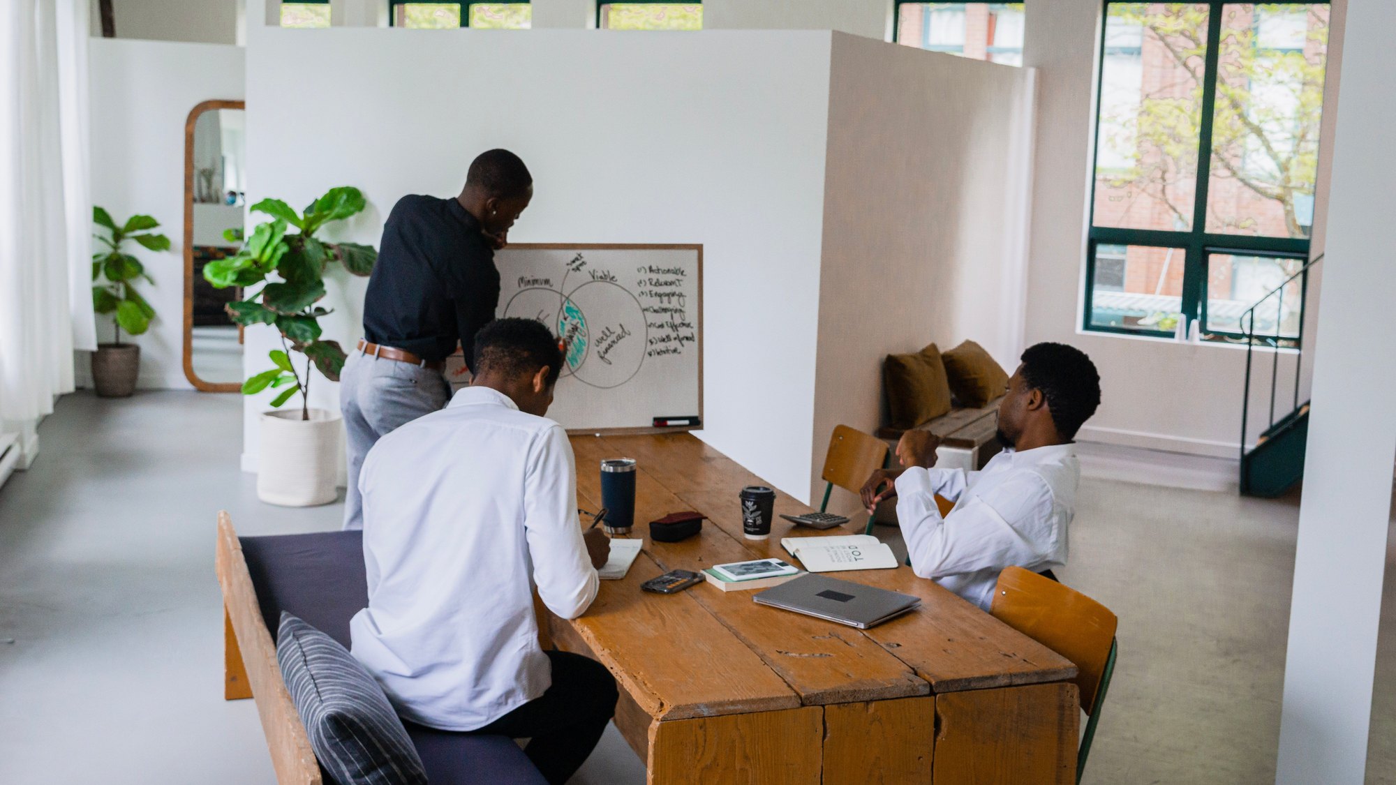 Three colleagues planning at a wooden table while one sketches on a whiteboard.