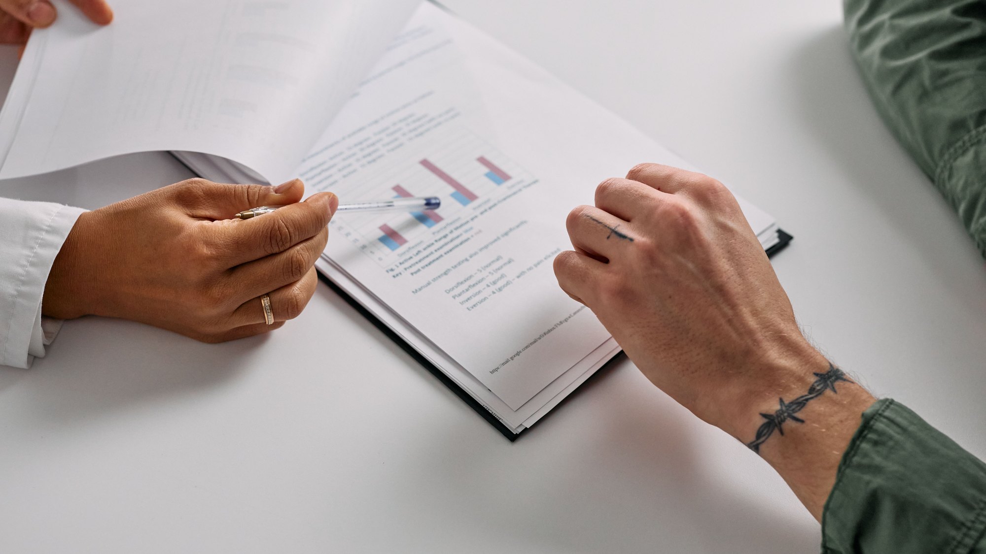 Two people going through a printed report together, one pointing at a chart with a pen.