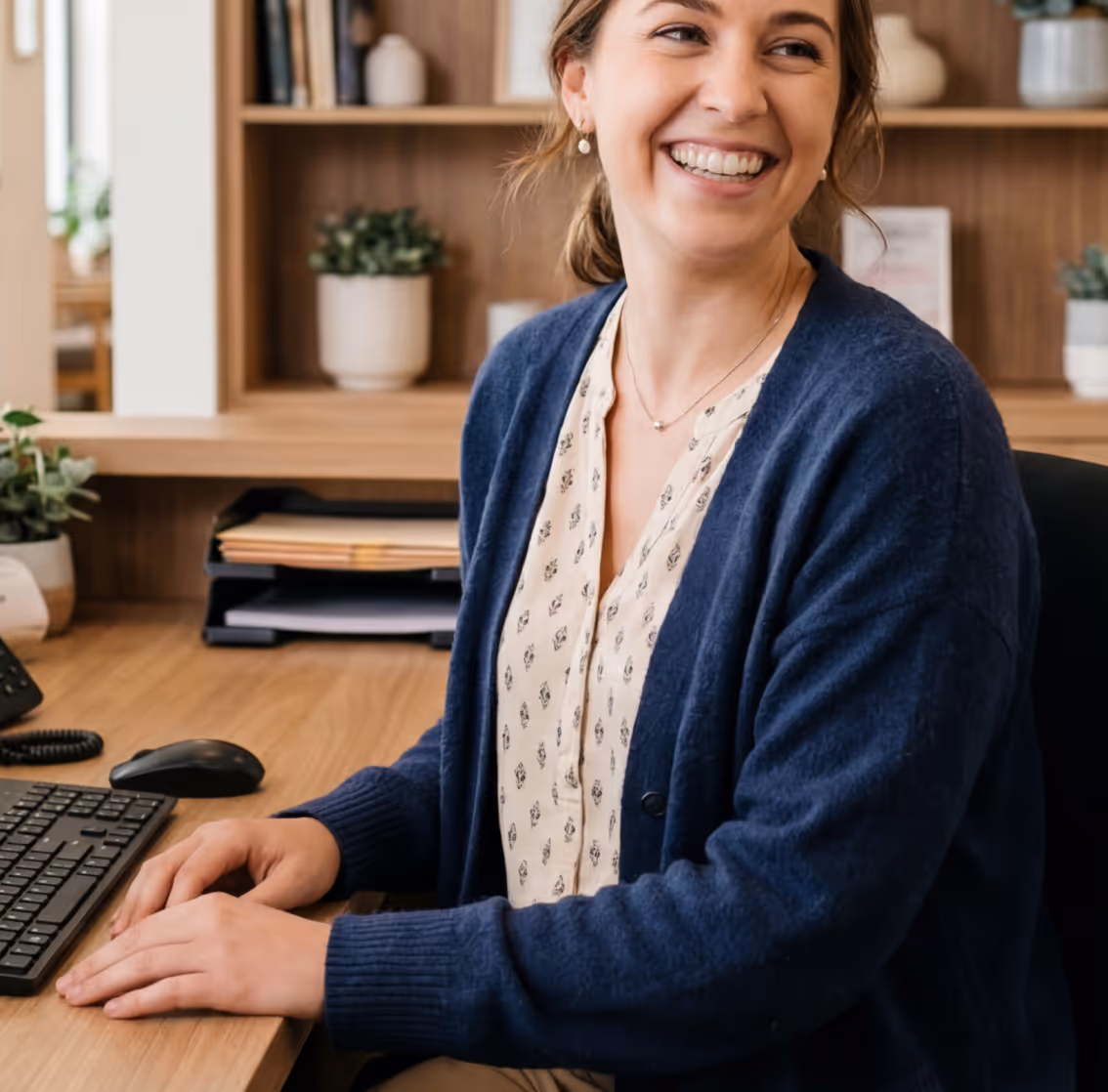 Clinic receptionist smiling at desk with AI assistant managing patient messages and calls