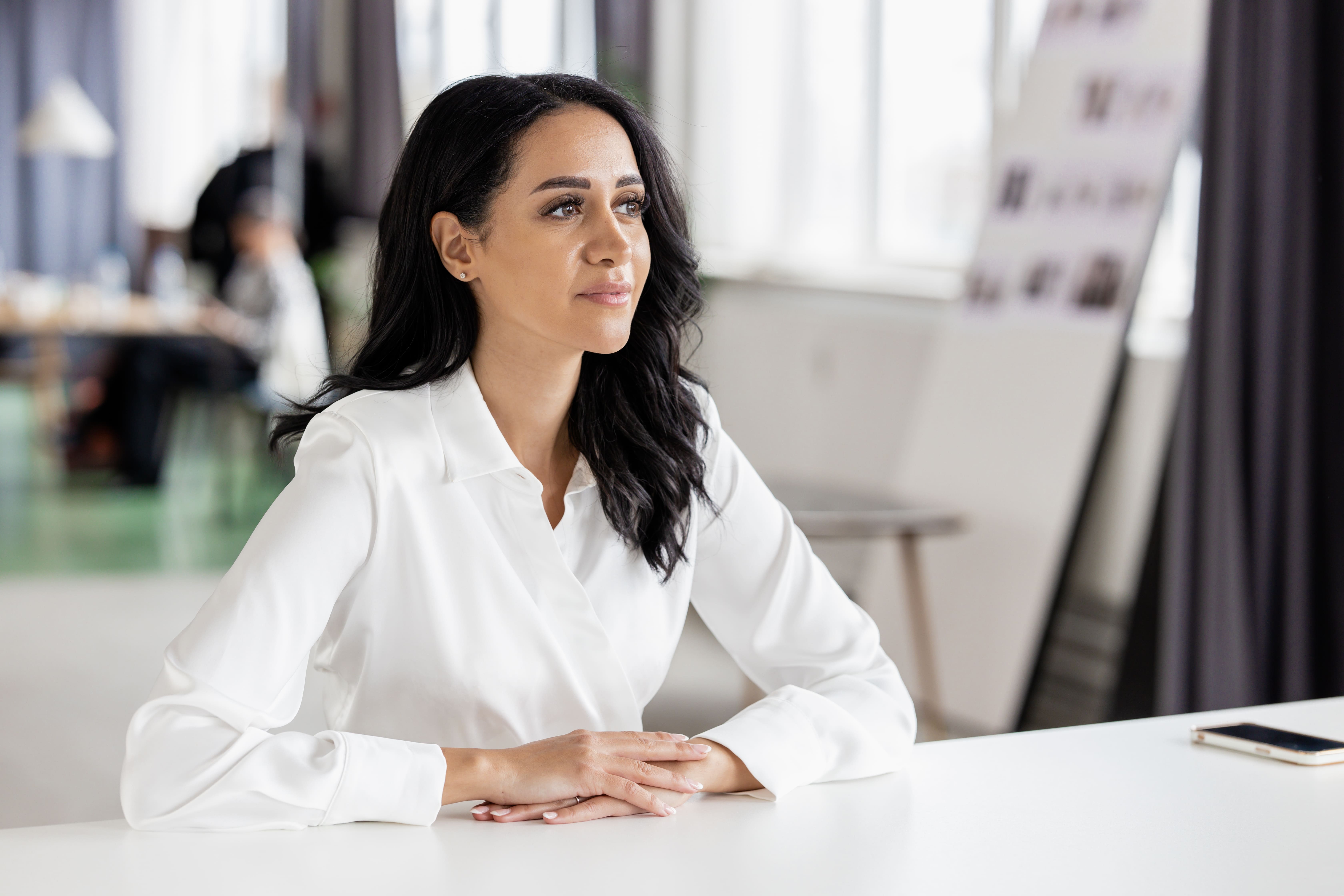 Person with short bob haircut wearing a white pleated-back shirt facing away against a dark background.