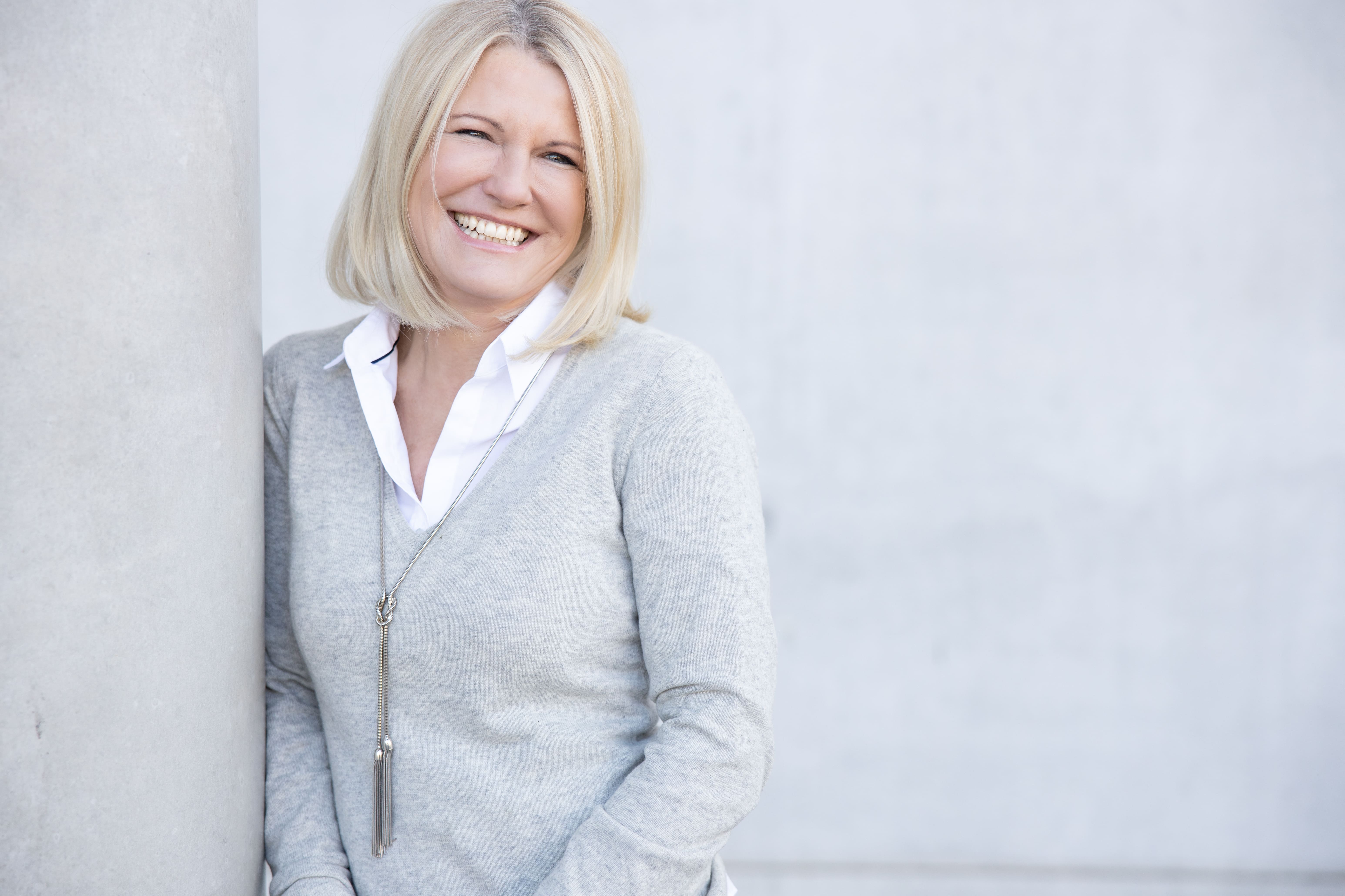 Person with short bob haircut wearing a white pleated-back shirt facing away against a dark background.