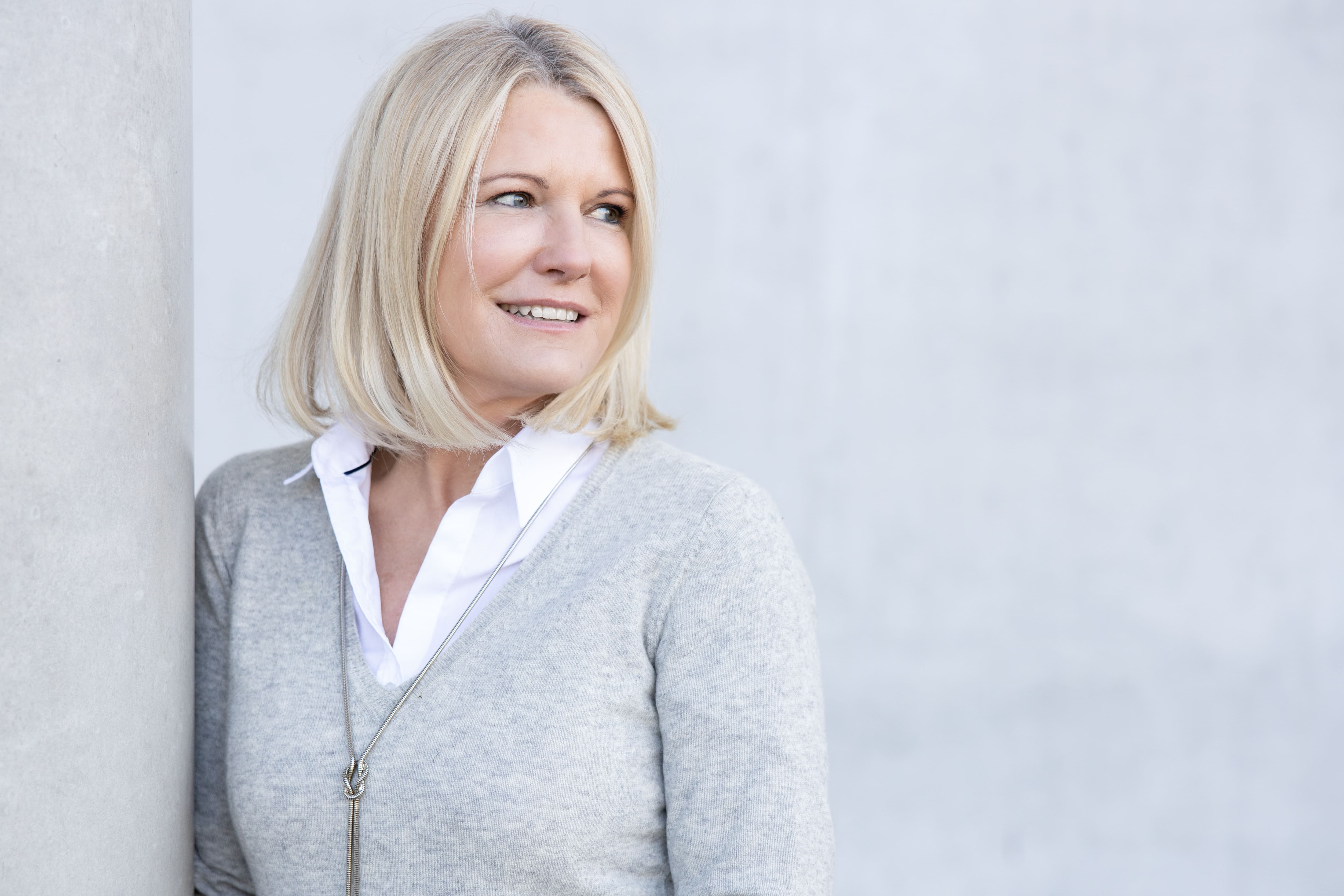 Person with short bob haircut wearing a white pleated-back shirt facing away against a dark background.