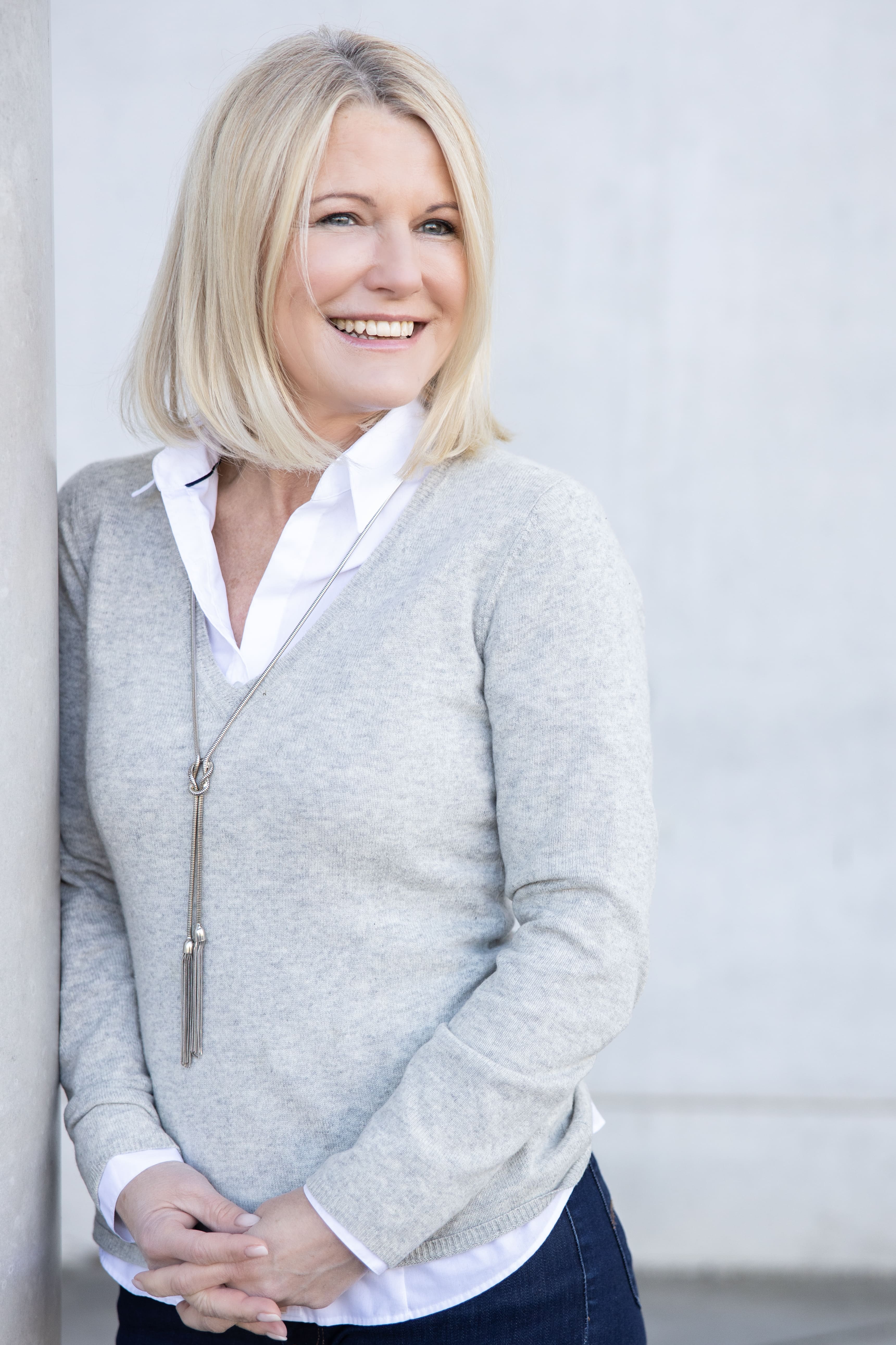 Person with short bob haircut wearing a white pleated-back shirt facing away against a dark background.