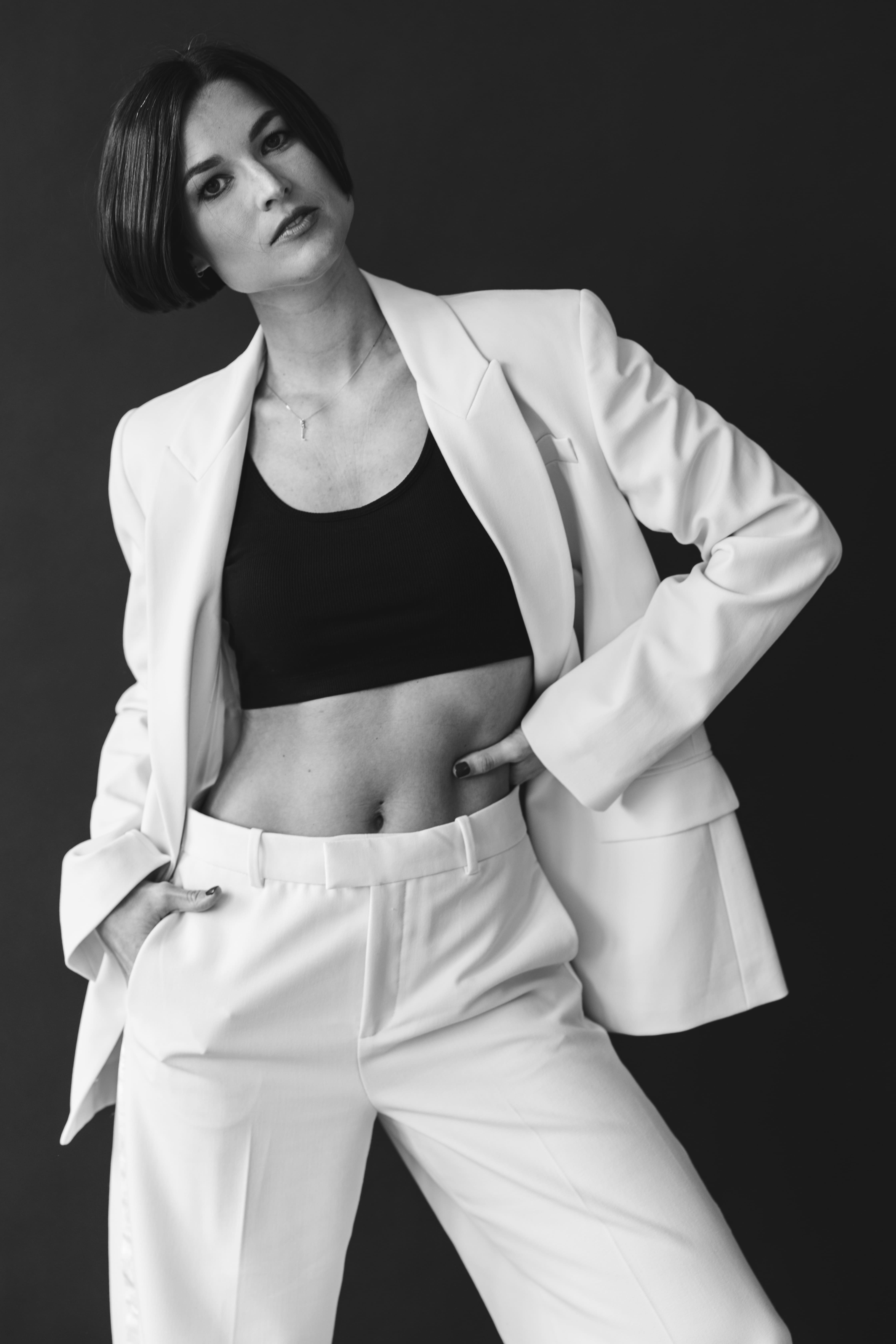 Person with short bob haircut wearing a white pleated-back shirt facing away against a dark background.